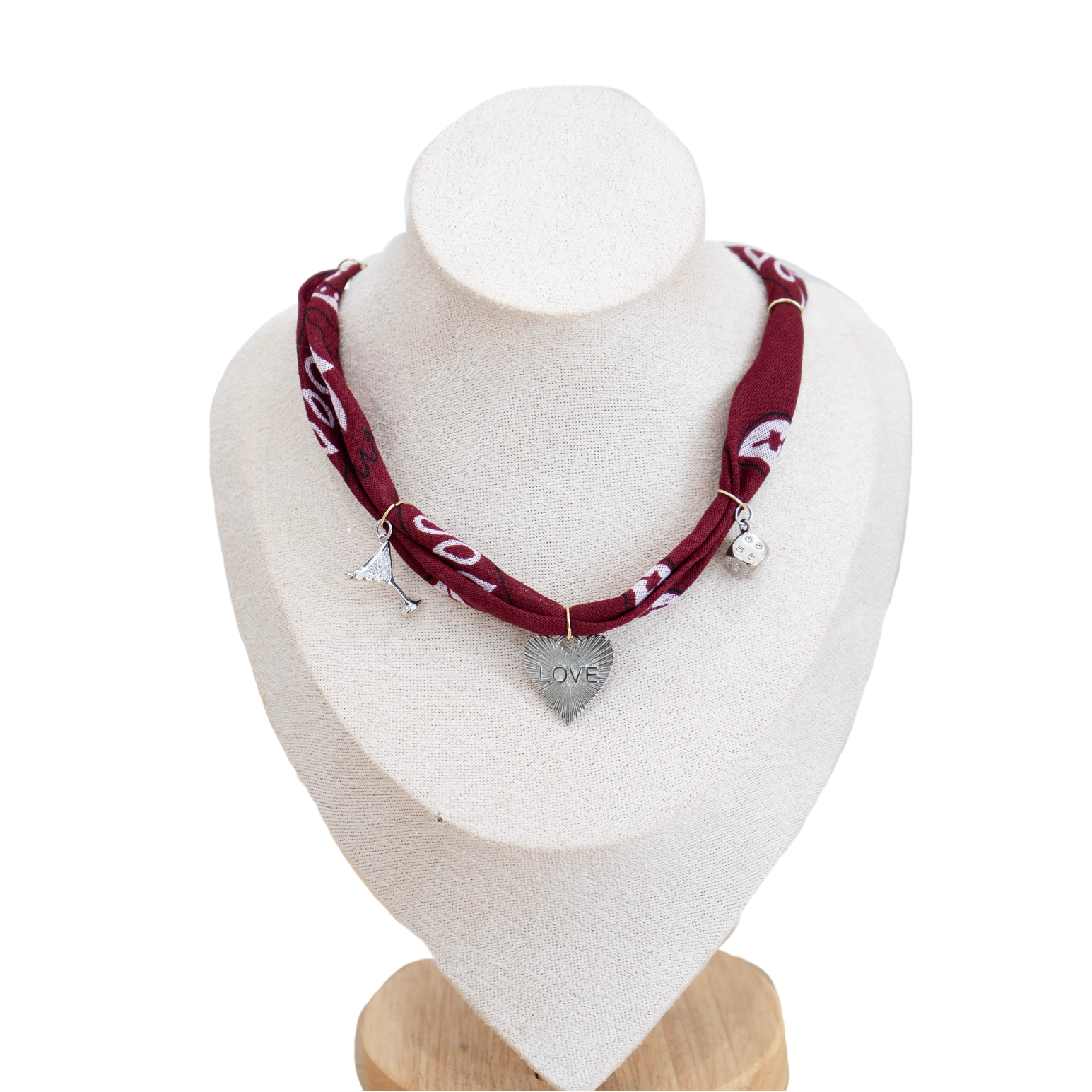 A double-layered maroon bandana necklace with white printed graphics and silver charms, displayed on a cream-colored mannequin bust.