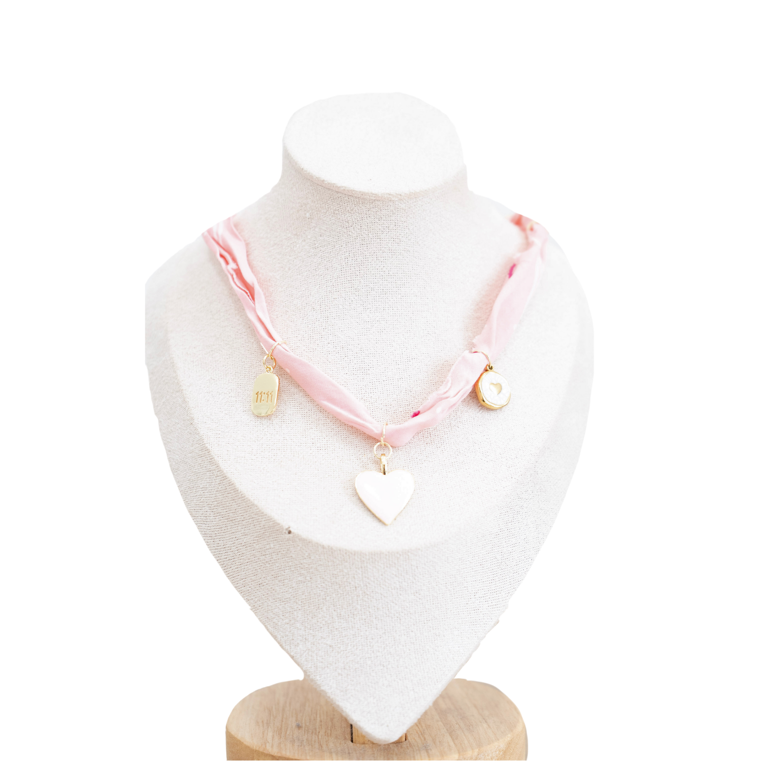 A pink ribbon bandana necklace with a white heart pendant and small gold charms, displayed on a white jewelry bust against a white background.
