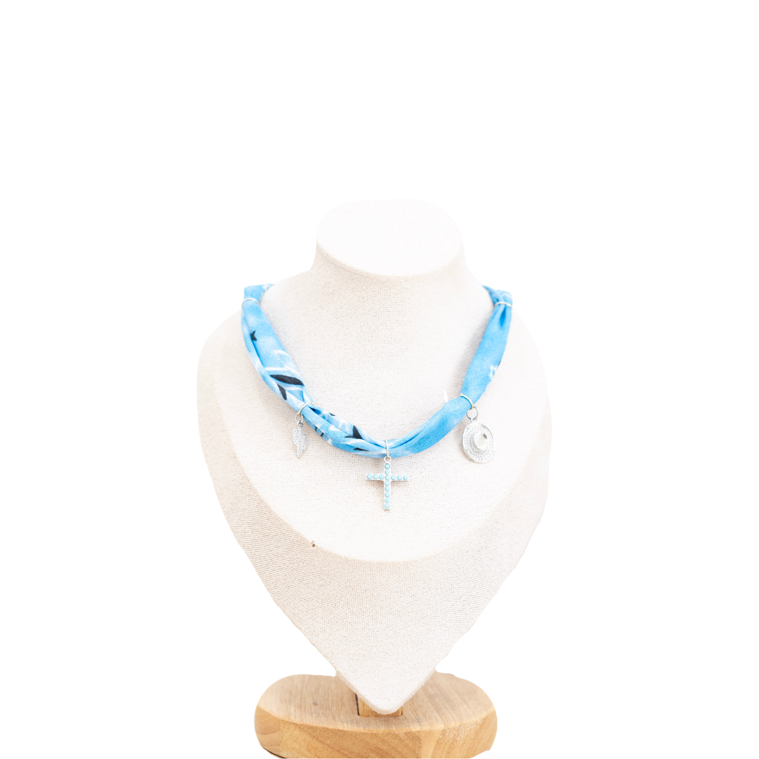 A light blue patterned scarf necklace with silver-tone charms, displayed on a cream-colored fabric jewelry bust with a wooden base against a white background.