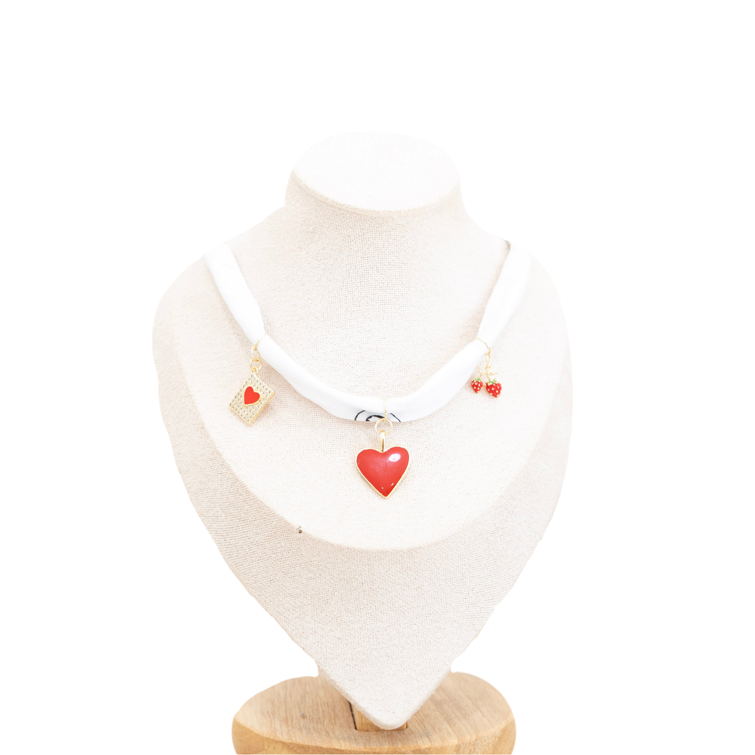 A white bandana necklace with red heart charms and small gold-toned details, displayed on a cream jewelry bust against a white background.