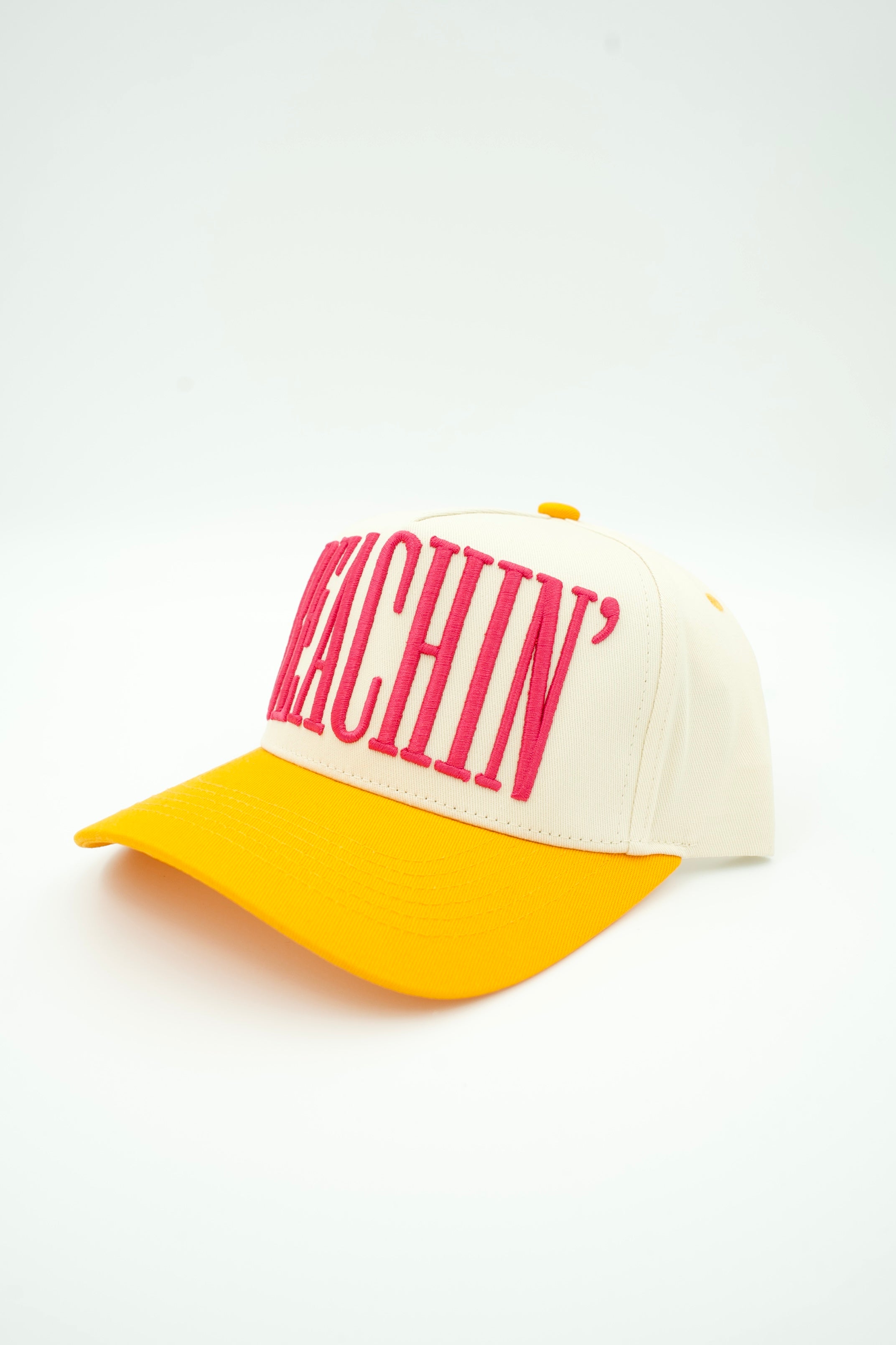 A two-tone baseball cap with a cream-colored crown and a bright yellow brim, featuring the word 'BEACHIN' embroidered in bold pink letters across the front.
