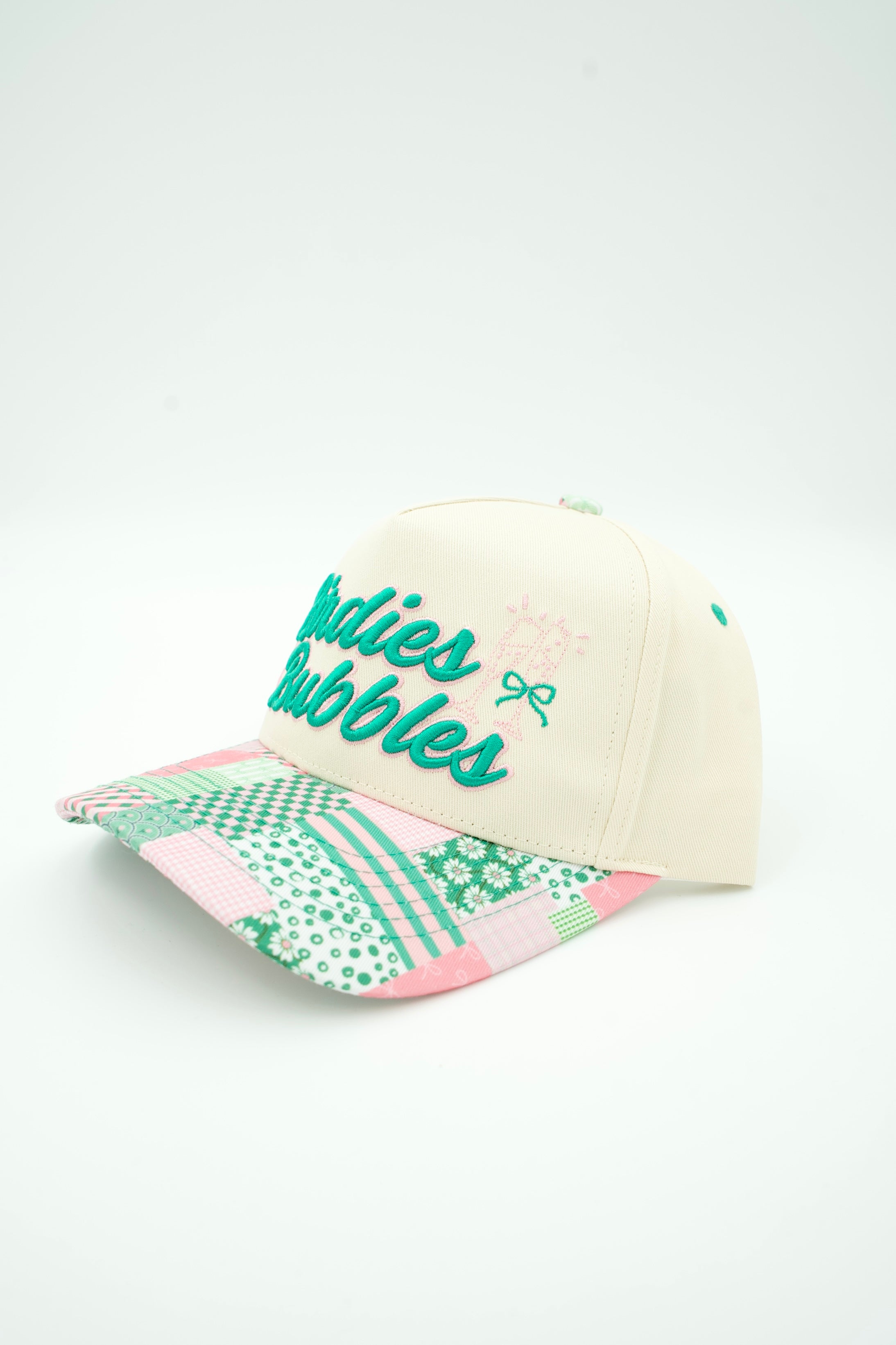 A baseball cap with a cream-colored crown, teal embroidered text reading 'Babies Bubbles' on the front, and a patterned brim featuring green and pink geometric designs, set against a plain white background.