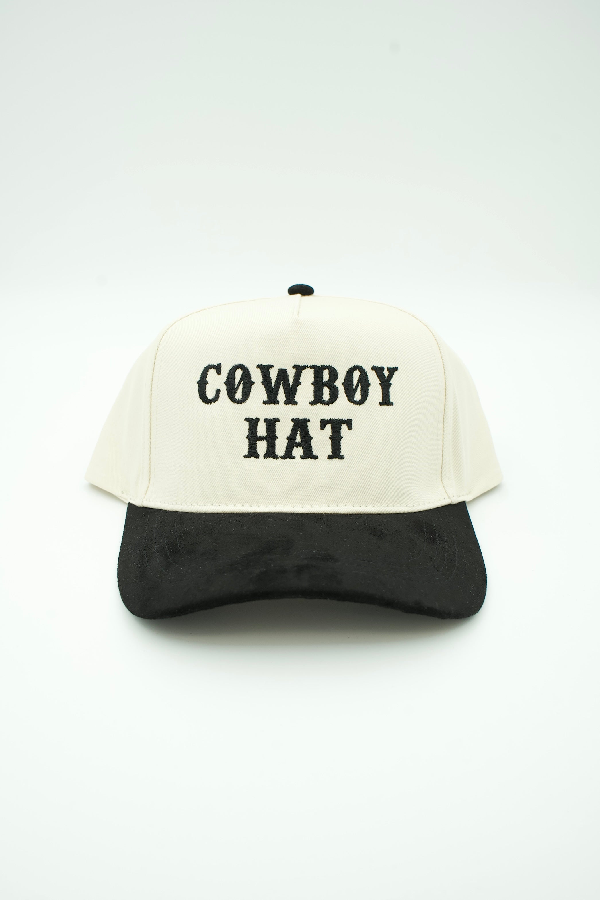 A two-tone baseball cap with an off-white crown and a black curved brim, featuring the words 'COWBOY HAT' embroidered in black on the front. The cap is photographed against a seamless white studio background.