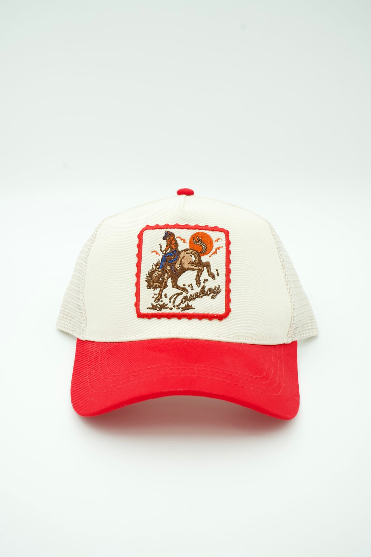 Front image of canvas trucker hat with embroidered "COWBOY" and a cowboy on a bucking horse with a sunset in the background with a red bill