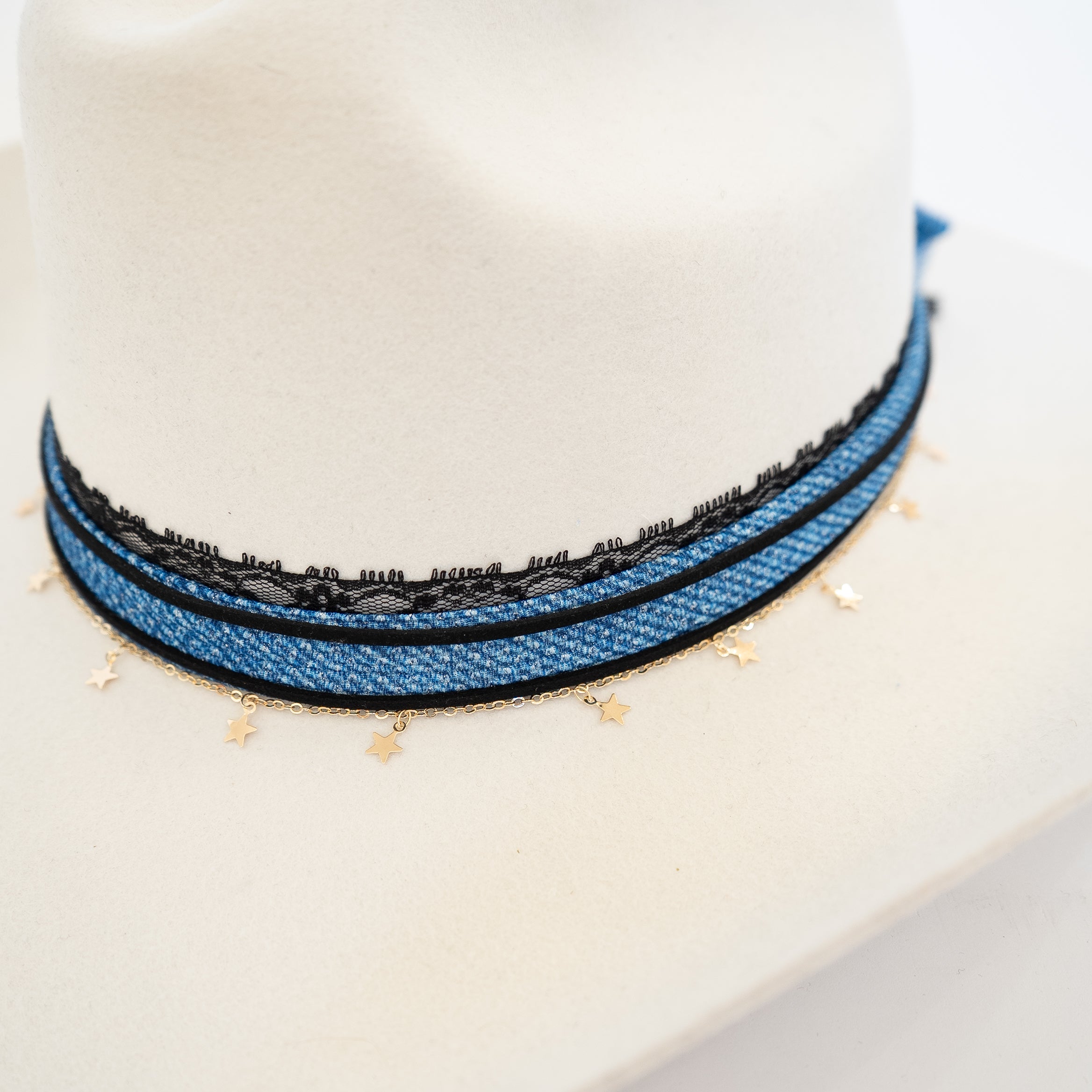 A close-up of a blue braided cord necklace with black lace trim and small gold star charms, displayed on a white mannequin bust.