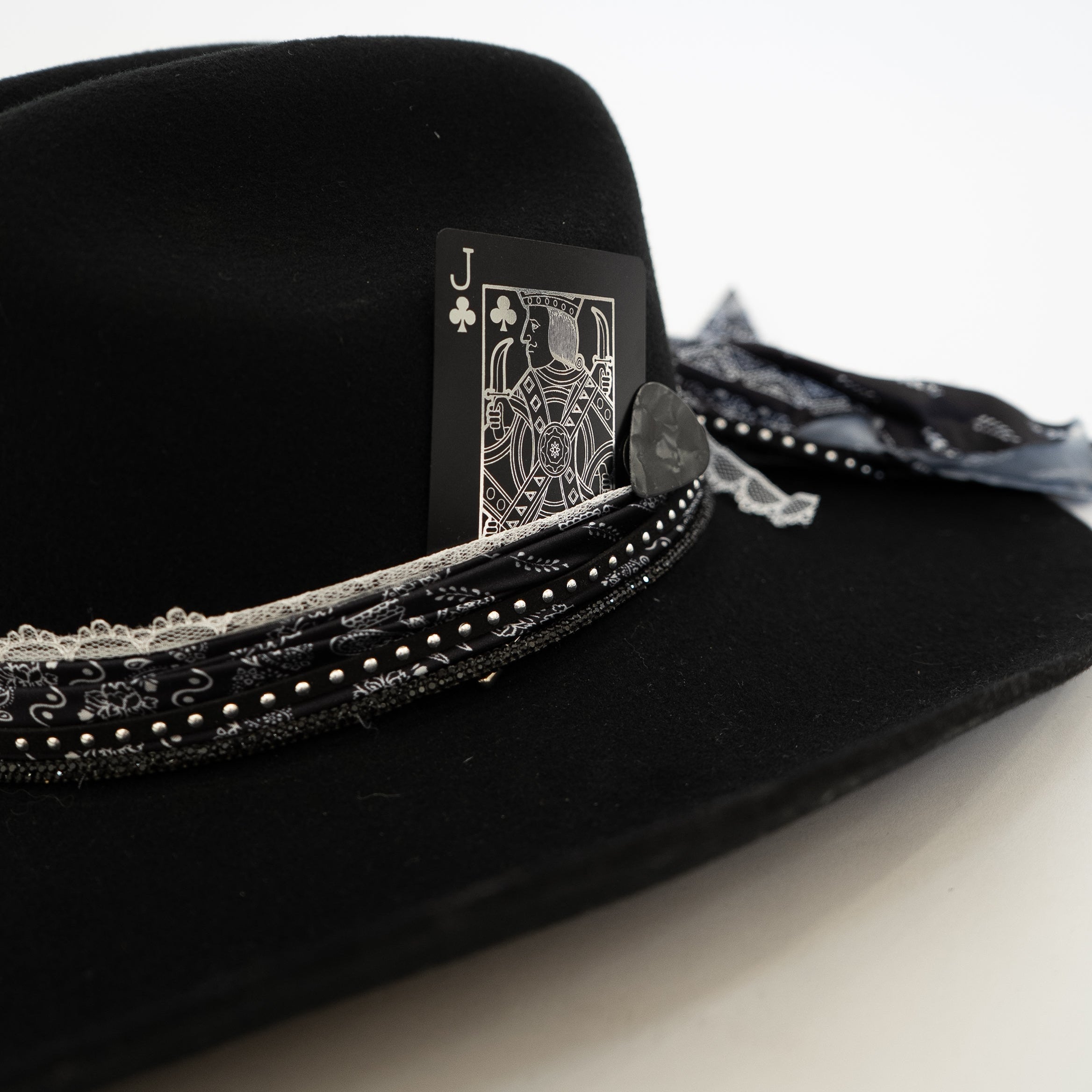 A black felt cowboy hat decorated with a black and silver beaded band, a small gray stone, and a playing card jester design on the side, photographed against a plain white background.