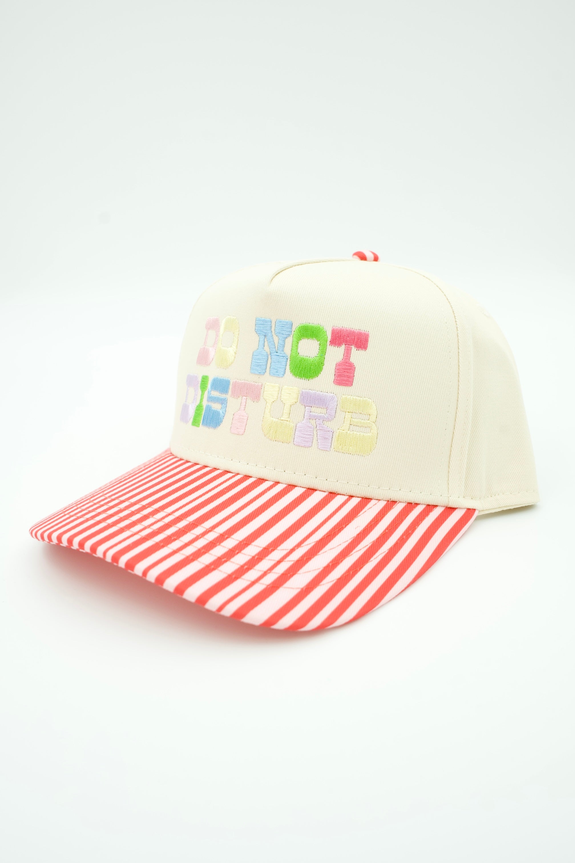 A cream-colored baseball cap with a red and white striped brim. The front of the cap features colorful embroidered text reading 'DO NOT DISTURB' in pastel shades of pink, green, blue, yellow, and purple.