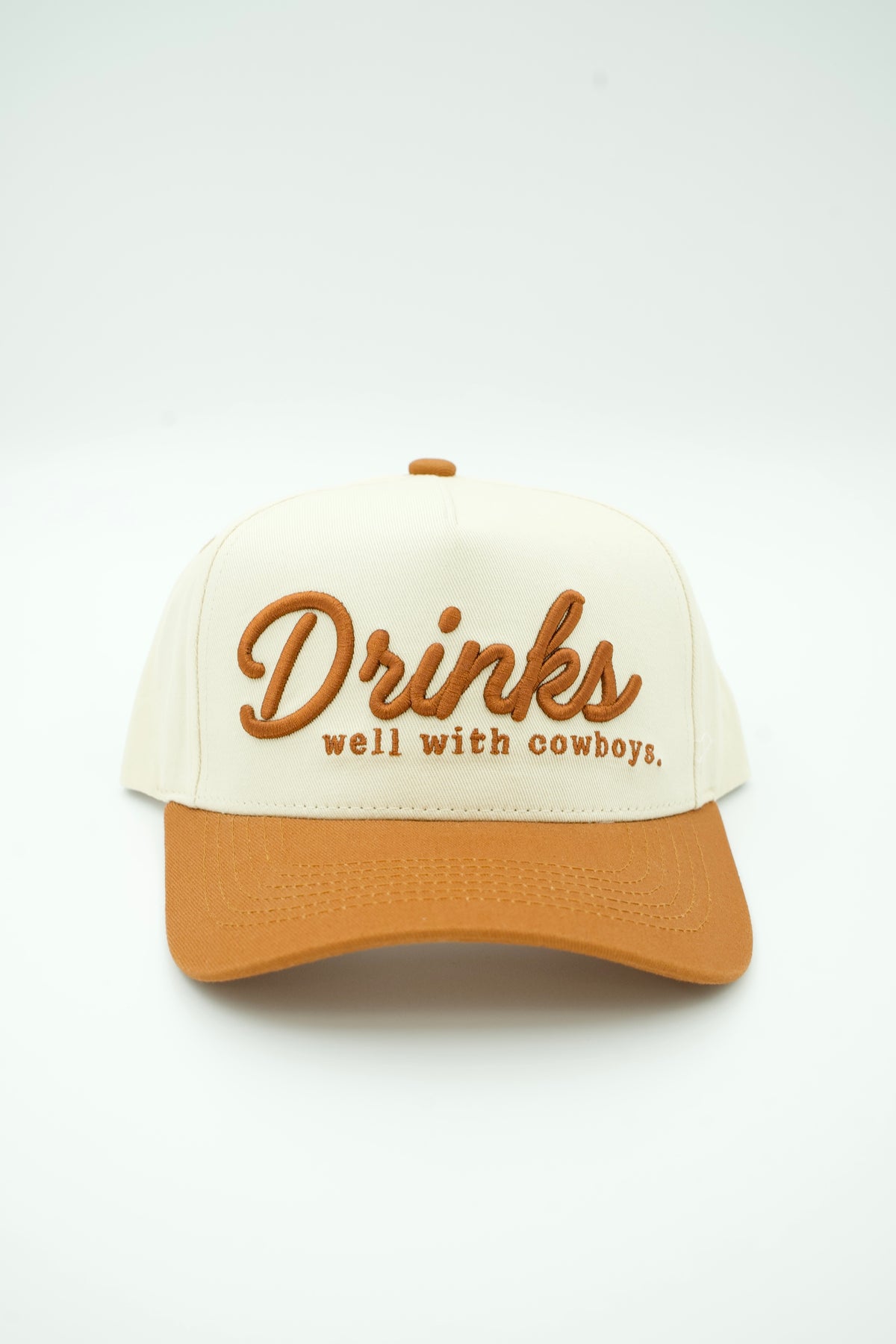 Front image of ivory canvas trucker hat with DRINKS WELL WITH COYBOYS embroidered in brown with brown bill