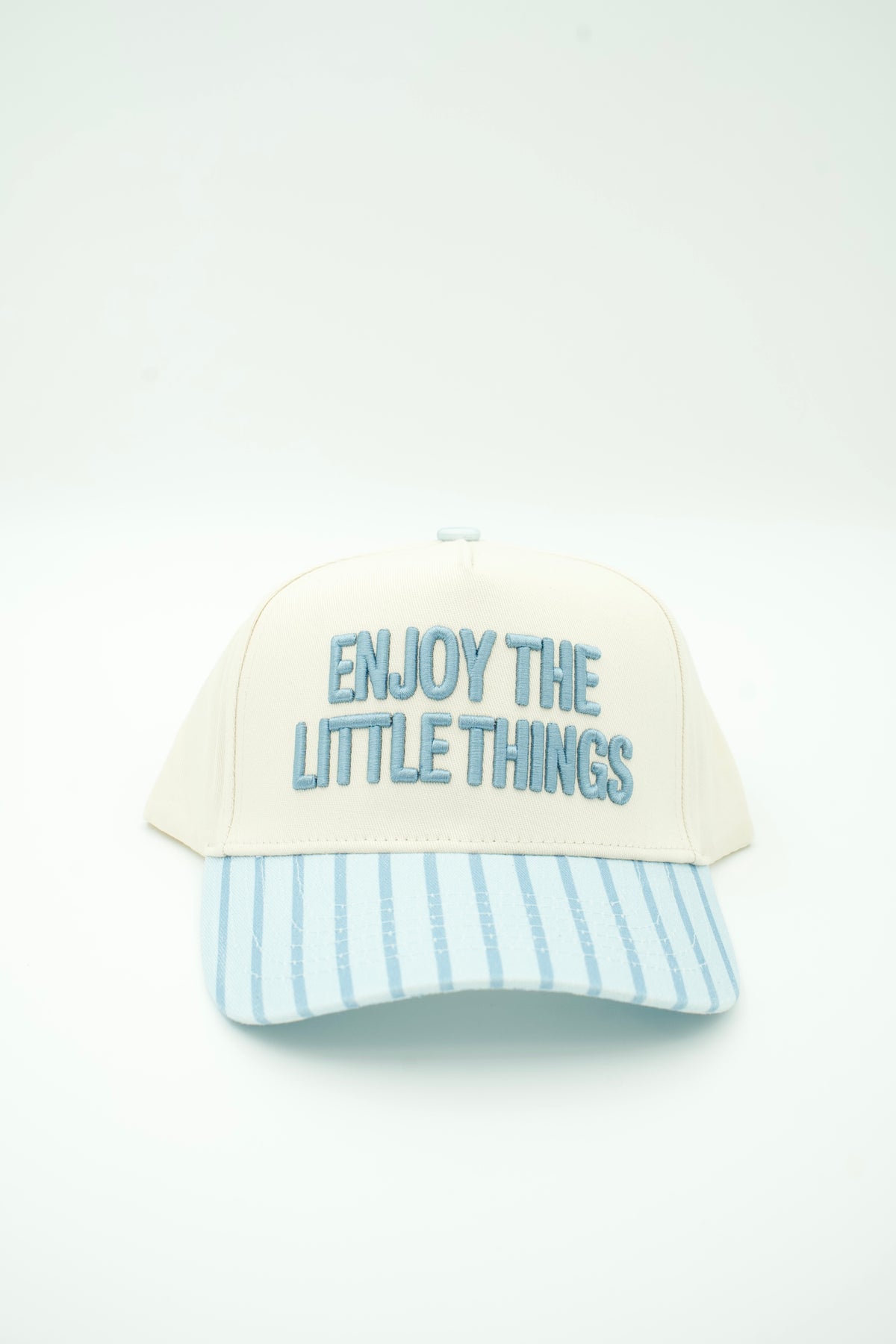 A cream-colored baseball cap with a light blue and white striped brim, featuring the embroidered text 'ENJOY THE LITTLE THINGS' in light blue on the front.