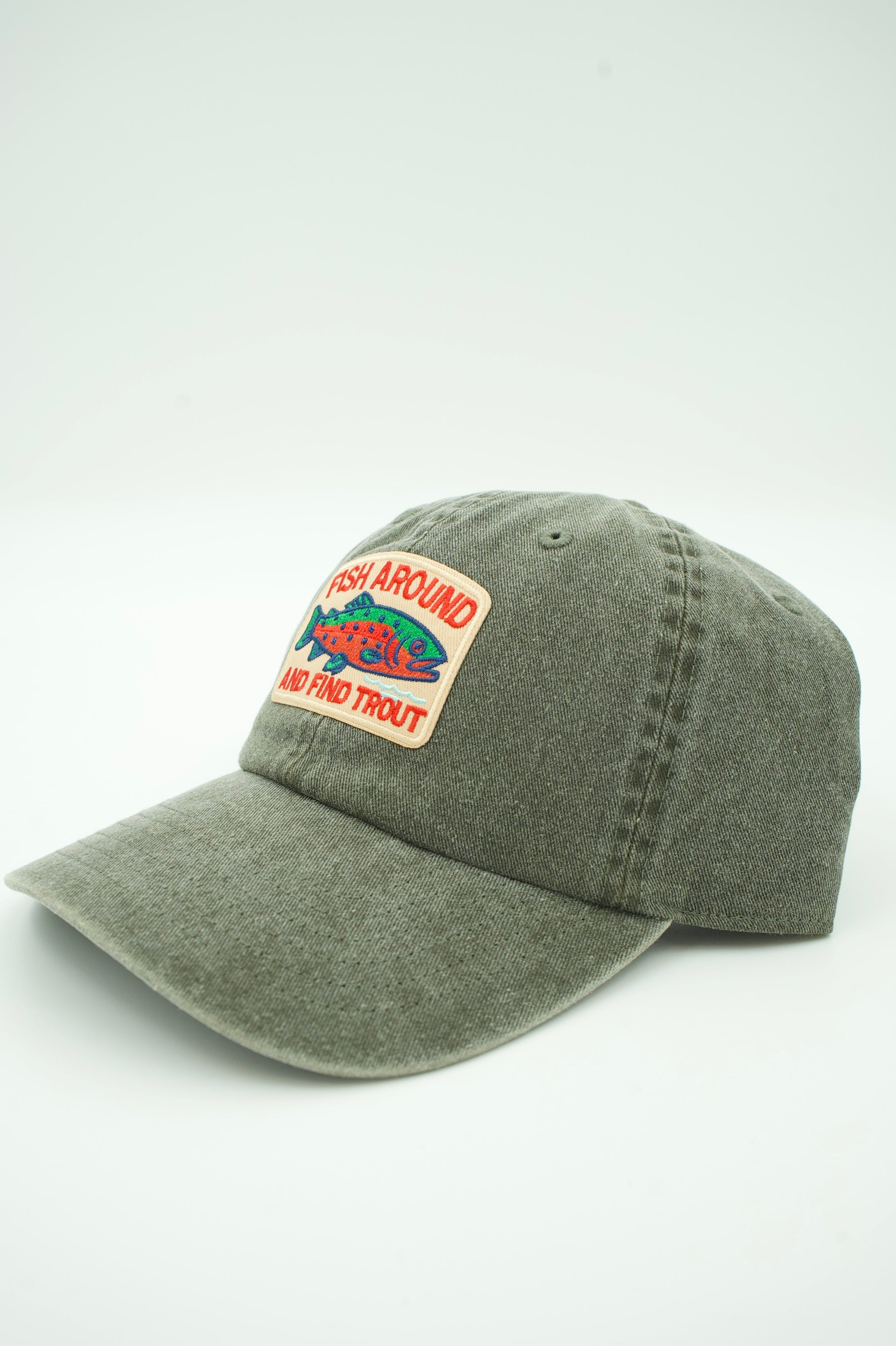 A washed canvas trucker hat with a front patch that reads 'FISH AROUND THE TROUT' and shows a red and green fish graphic, photographed on a light gray background.