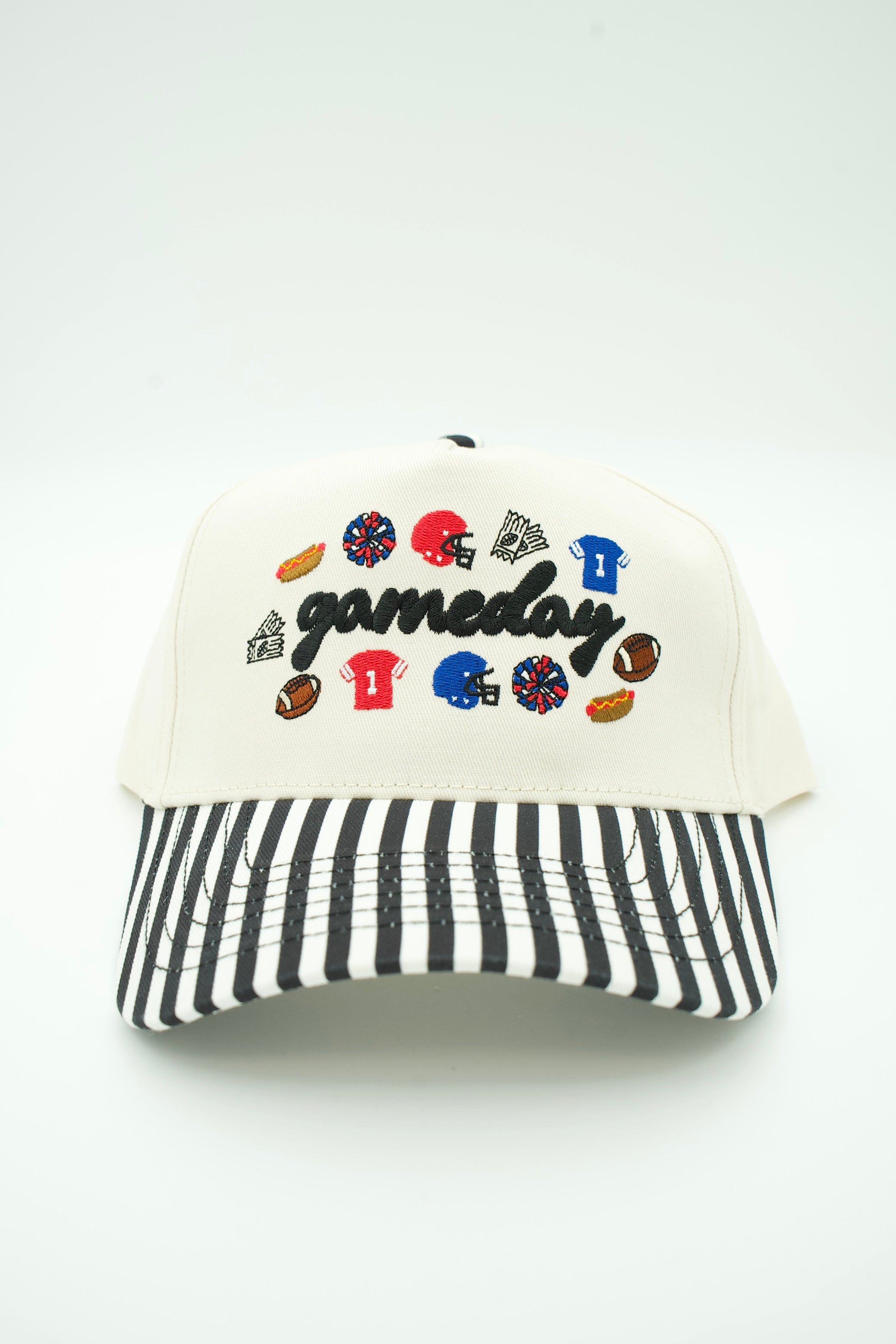 A baseball cap with an off-white crown, black and white striped brim, and 'gameday' embroidered in black script across the front, surrounded by small sports-themed patches. The cap is photographed on a clean white background.