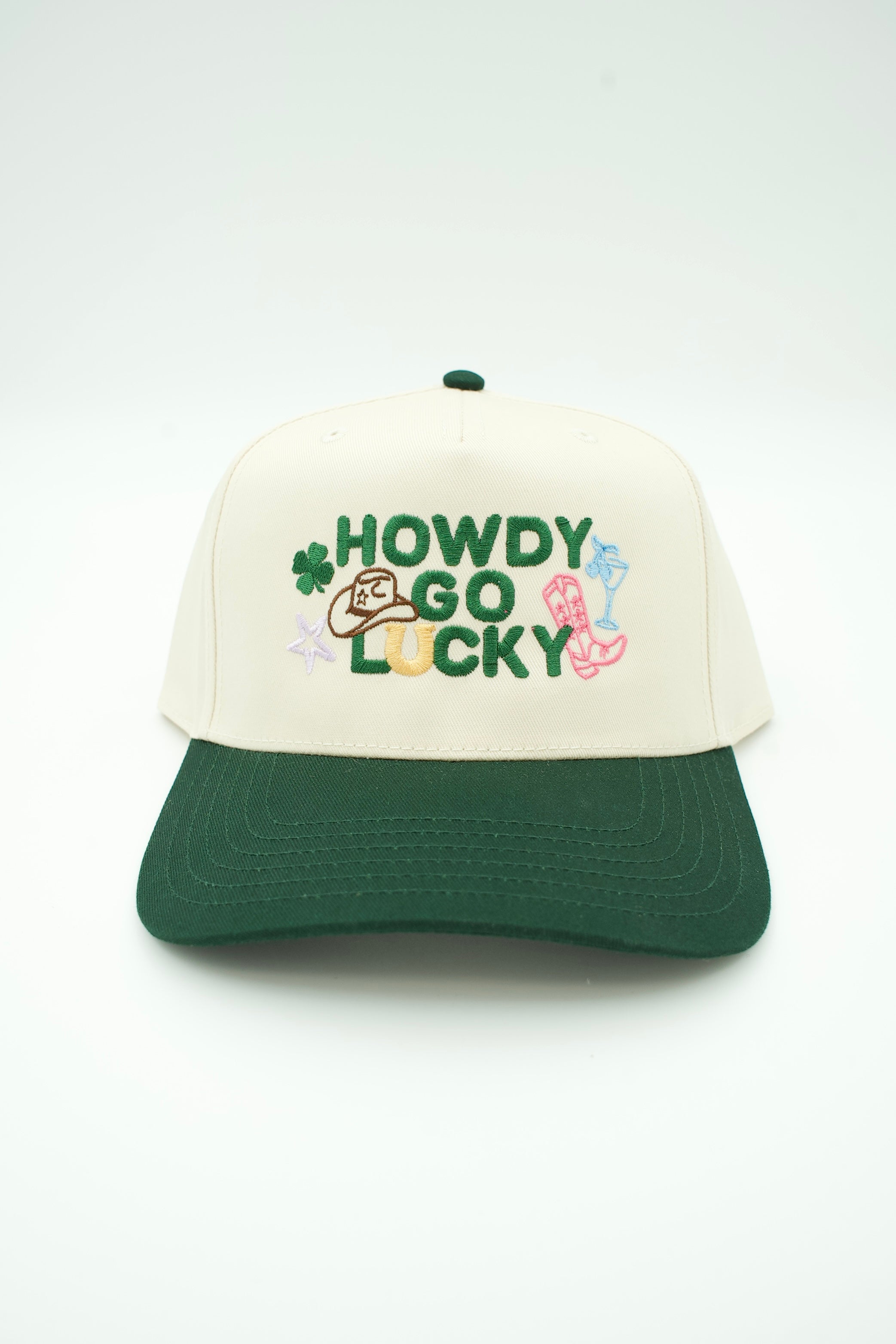 A lucky four leaf clover themed baseball cap with 'HOWDY GO LUCKY' embroidered in green on an off-white crown and a dark green visor.