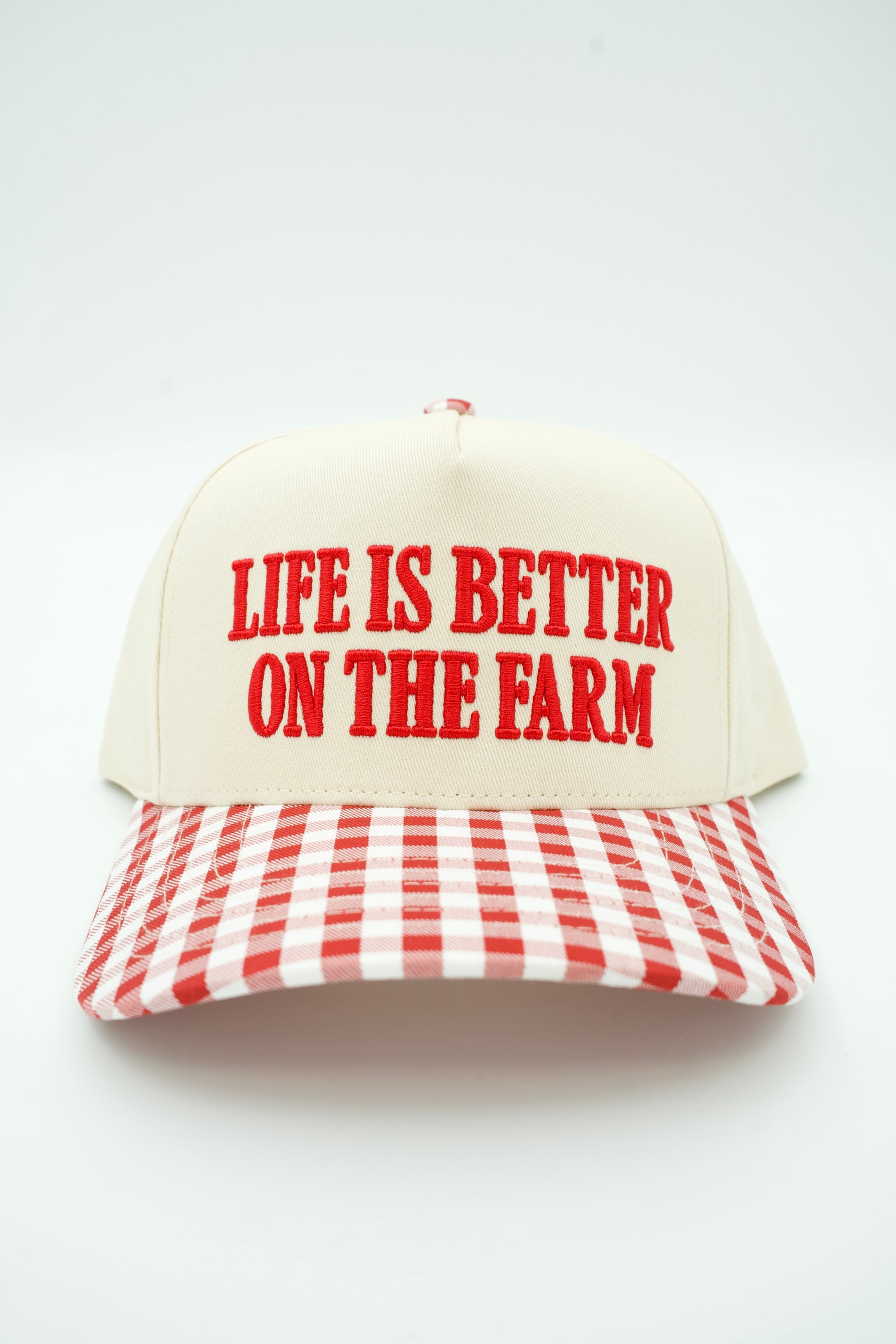 A baseball cap with an off-white crown and a red-and-white gingham brim, featuring the phrase 'LIFE IS BETTER ON THE FARM' embroidered in red across the front.