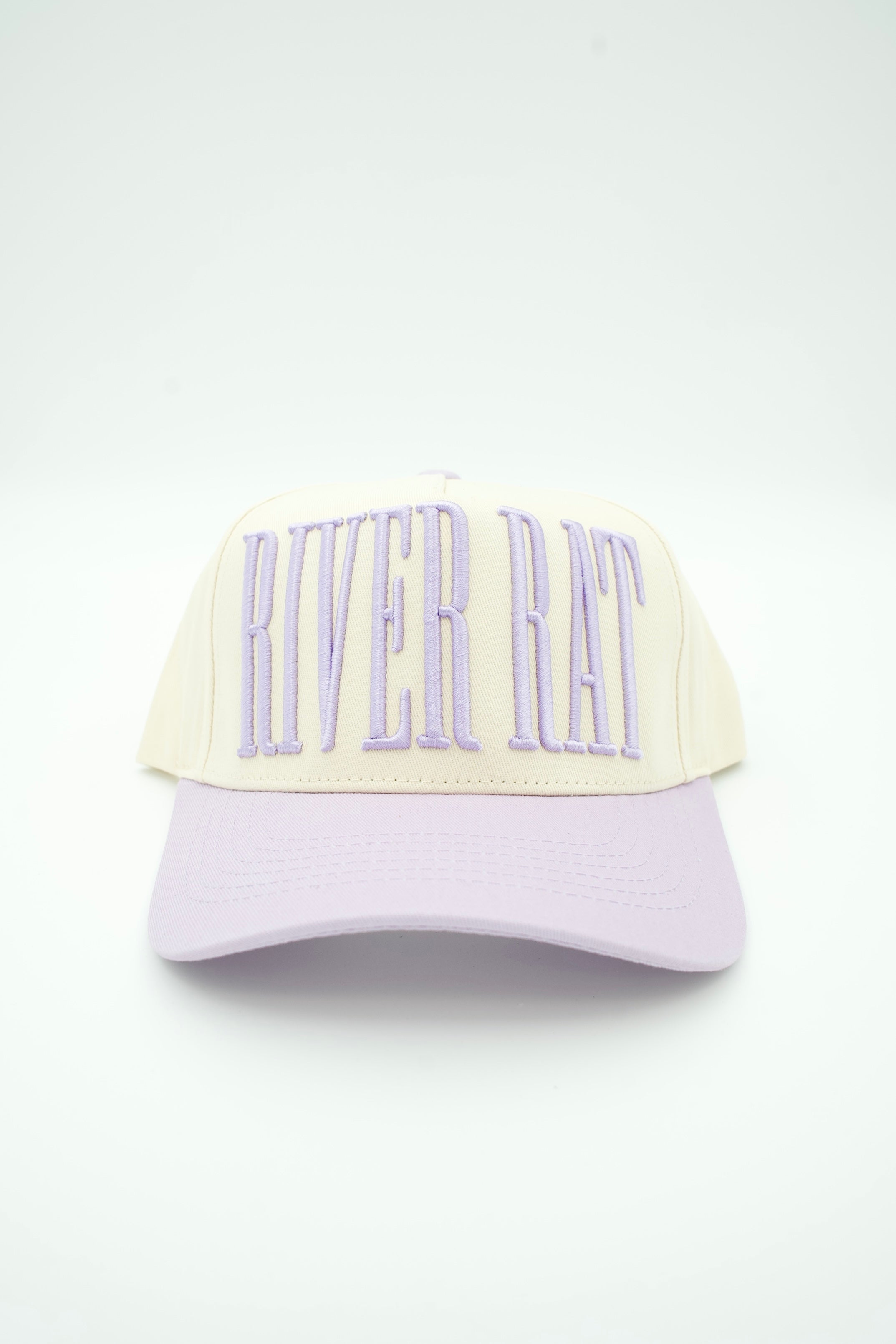 A cream-colored baseball cap with a light purple brim and light purple embroidered 'RIVER RAT' text on the front, set against a plain white background.
