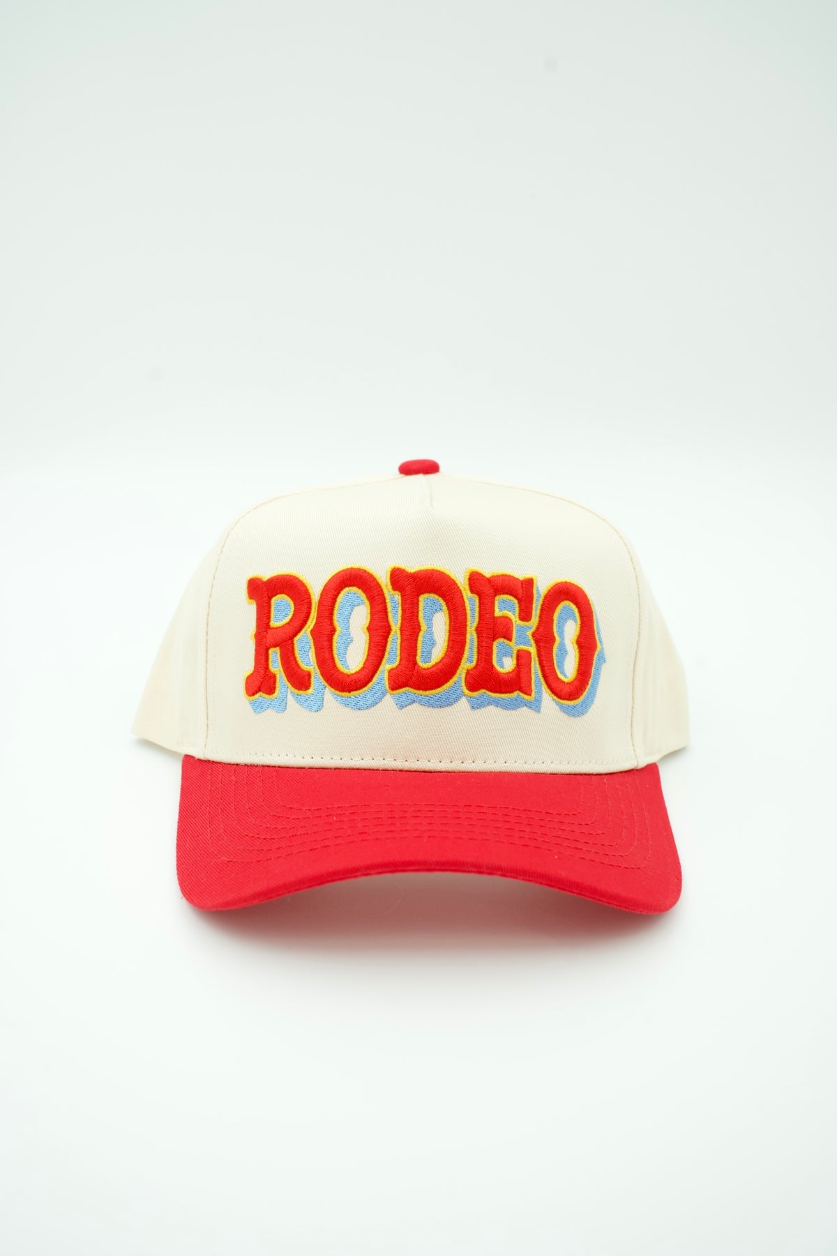 Front image of cream canvas trucker hat with RODEO embroidered in red and light blue with a red bill