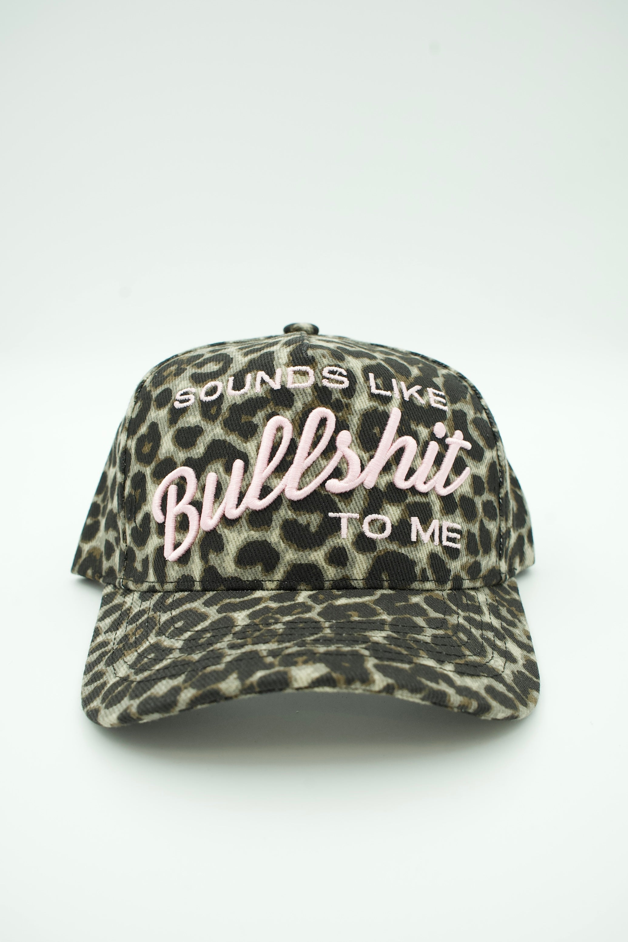 A baseball cap with a leopard print pattern in black and beige, featuring pink embroidered text on the front that reads 'SOUNDS LIKE Bullshit TO ME'.