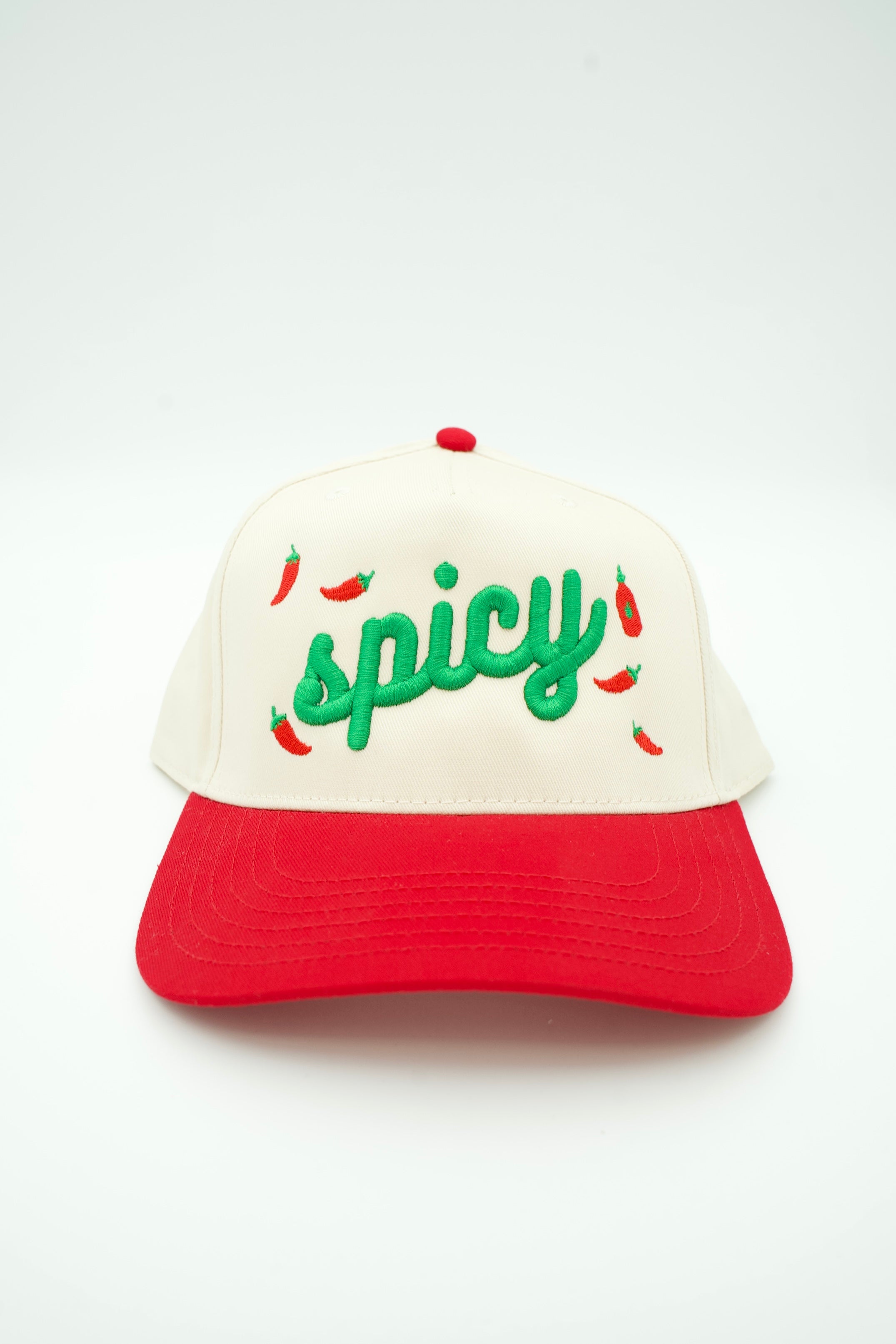 A two-tone trucker-style cap with an off-white crown and a red brim, featuring green embroidered 'spicy' script and small red chili pepper illustrations on the front.