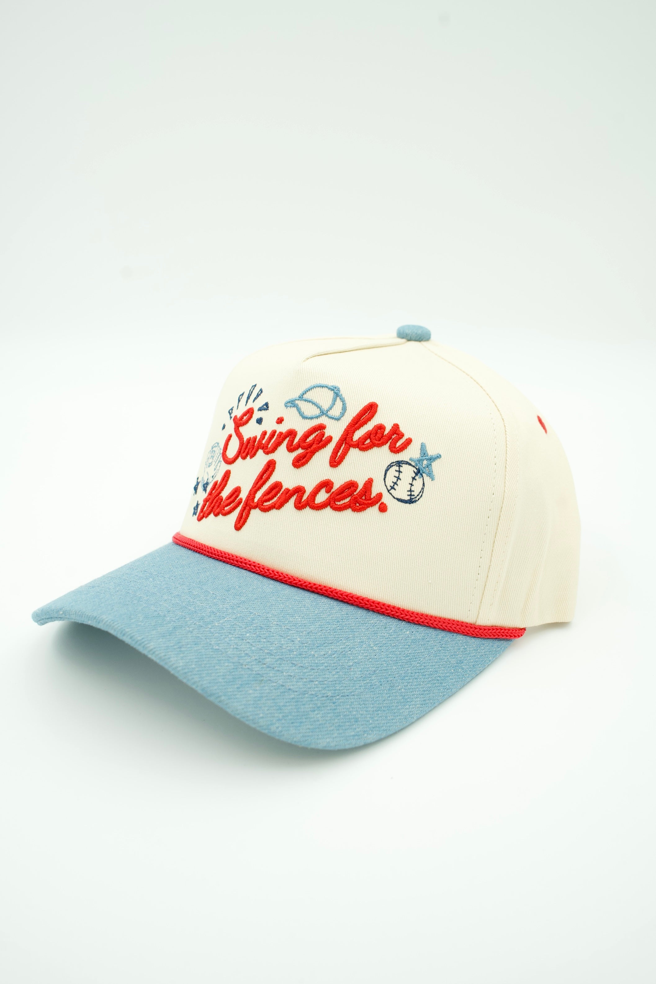 A baseball cap with an off-white crown, a light blue visor, and red embroidered text reading 'Swing for the fences' with small blue and red baseball-themed doodles.