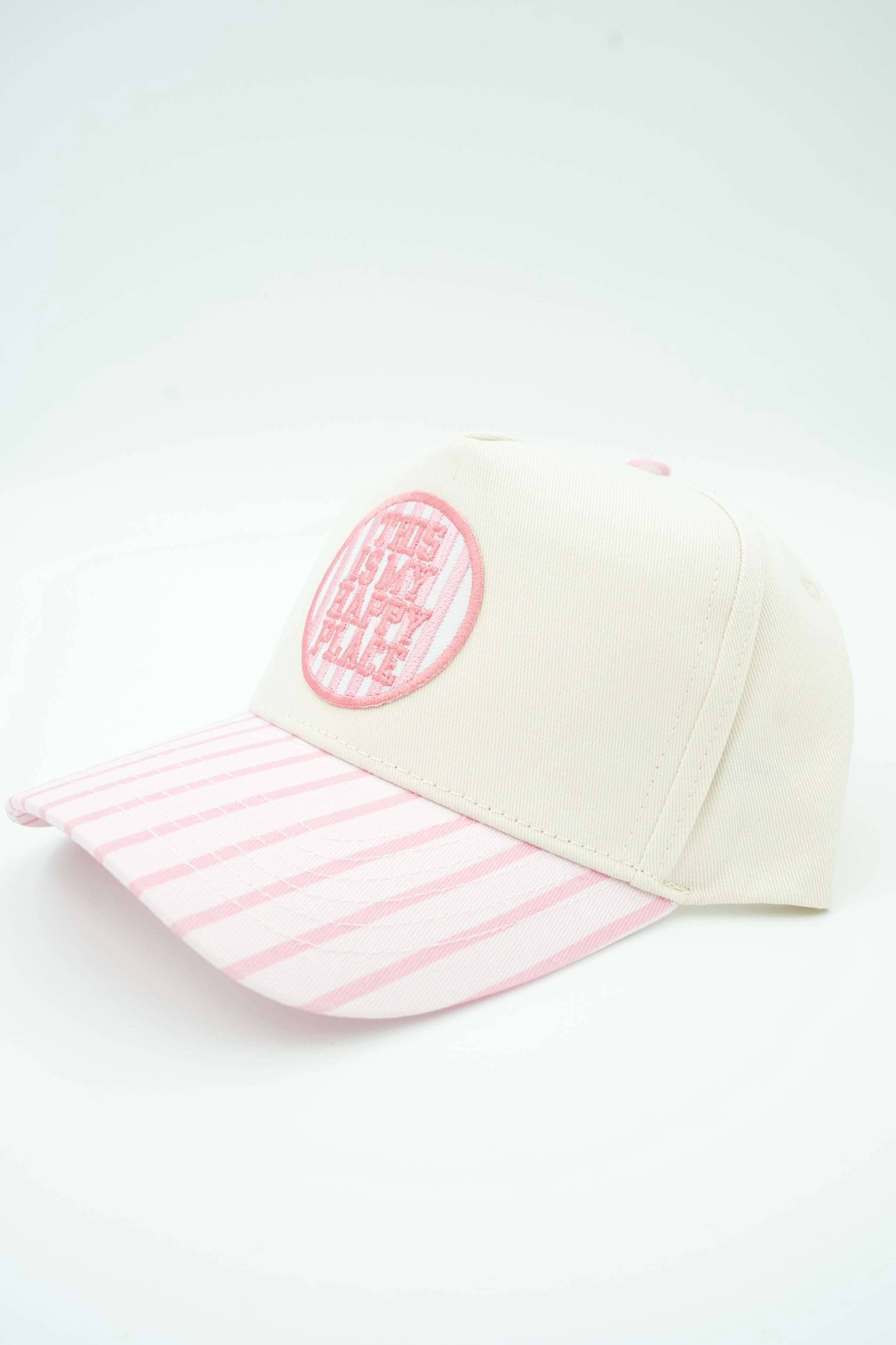 A baseball cap with an off-white crown and a pink and white striped brim, featuring a pink circular embroidered patch on the front.