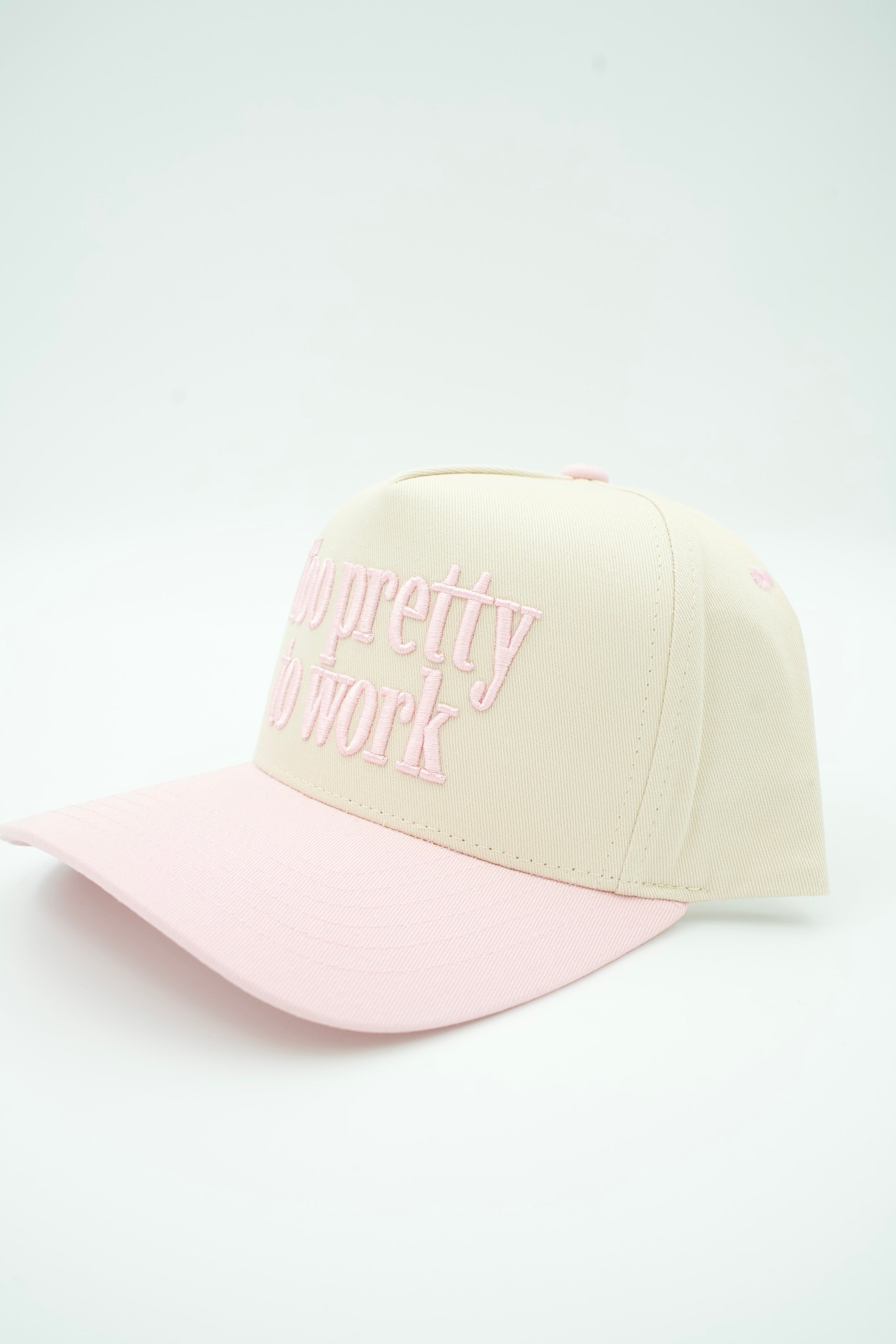 A baseball cap with a cream-colored crown and a light pink brim, featuring the phrase 'I'm pretty sure work' embroidered in pink on the front.