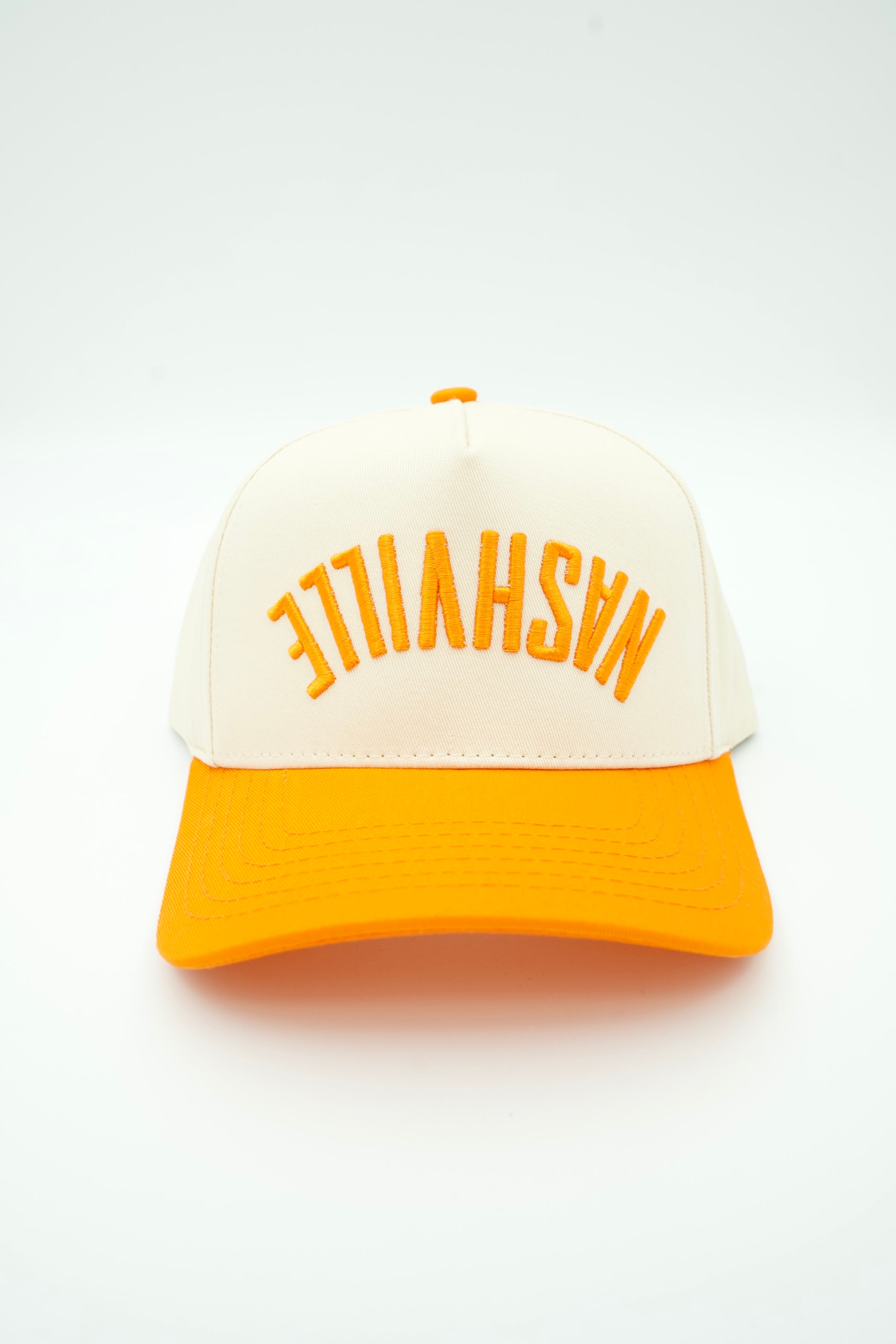 A two-tone trucker-style cap with an off-white crown and a bright orange brim, featuring the word 'NASHVILLE' embroidered in orange across the front.