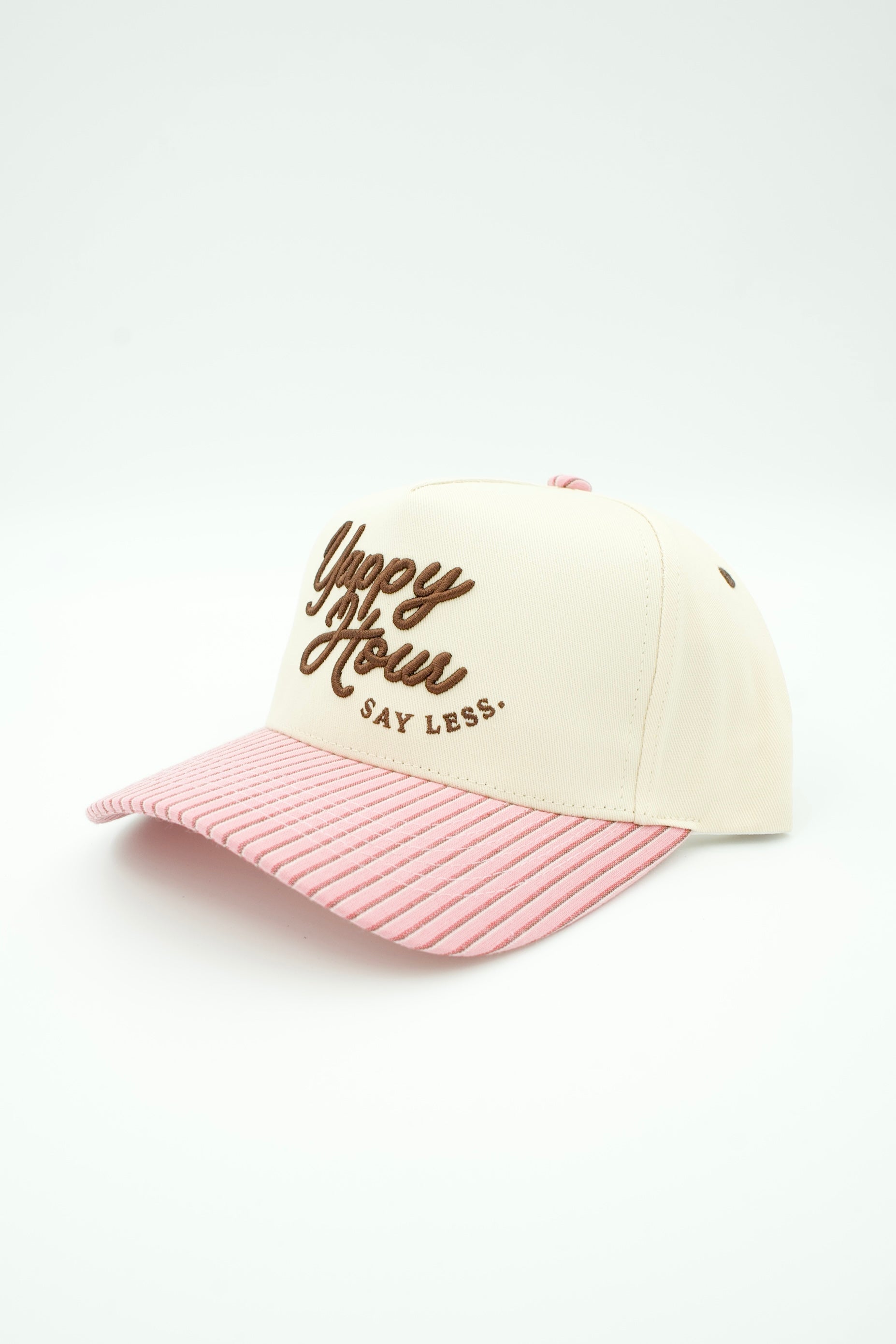 A trucker hat with an off-white crown, brown embroidered text reading 'Yippie Yoo-ho! SAY LESS.', and a pink and white striped brim, shown on a clean white background.