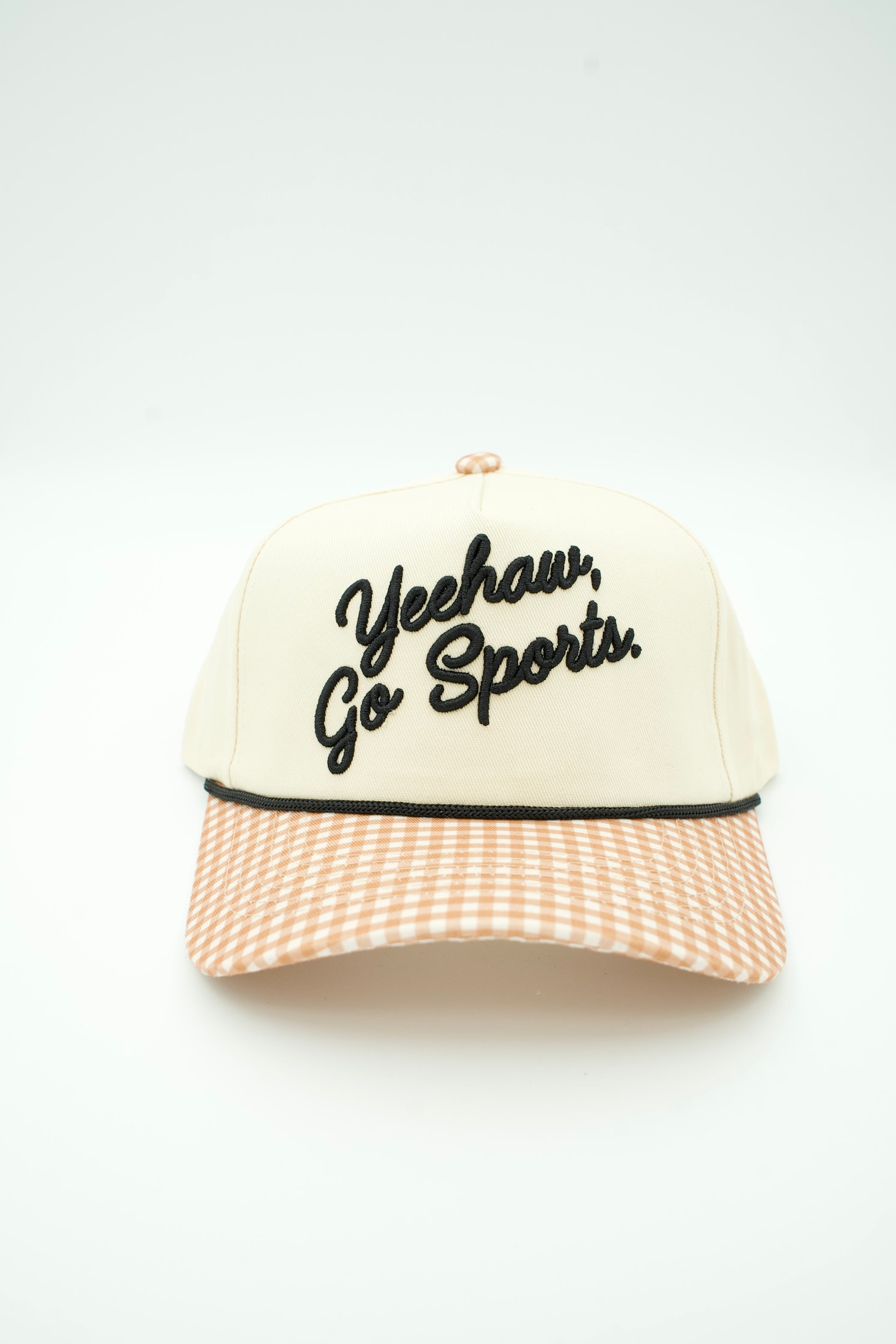 A cream-colored trucker-style cap with black embroidered text reading 'Yeehaw, Go Sports.' on the front, a black top button, and a peach-and-white gingham patterned visor.