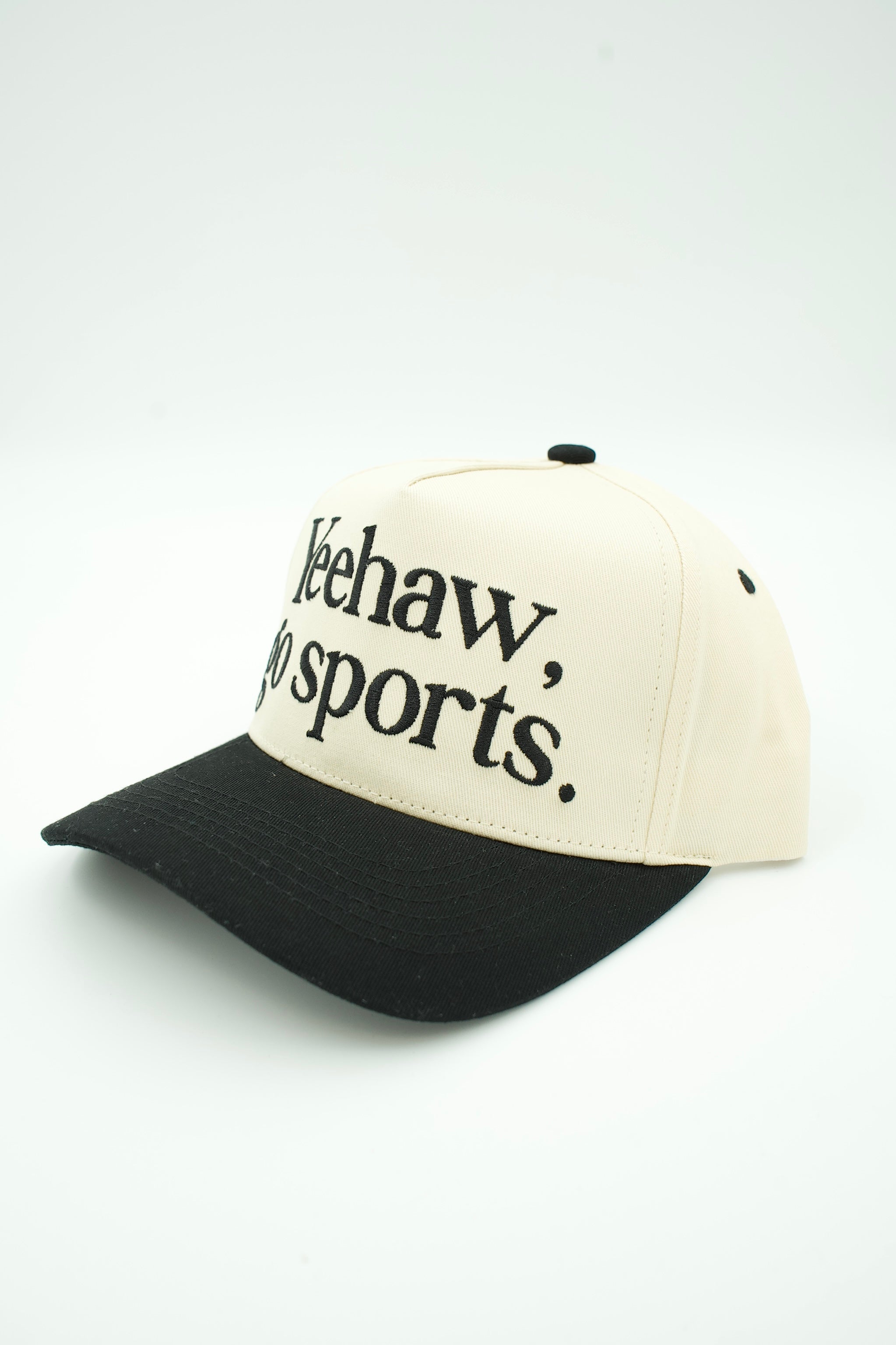 A two-tone baseball cap with an off-white crown and a black curved brim, featuring the text 'Keehaw, do sports.' embroidered in black on the front panel.