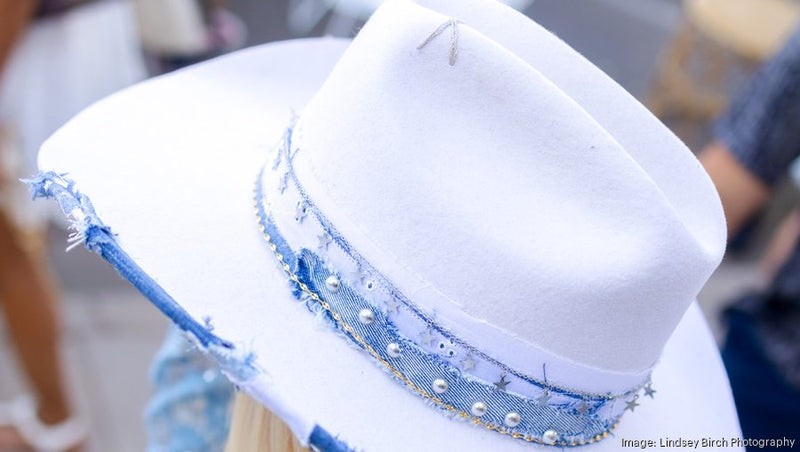 Picture of a white cowboy hat with blue ribbon and pearl embellishments