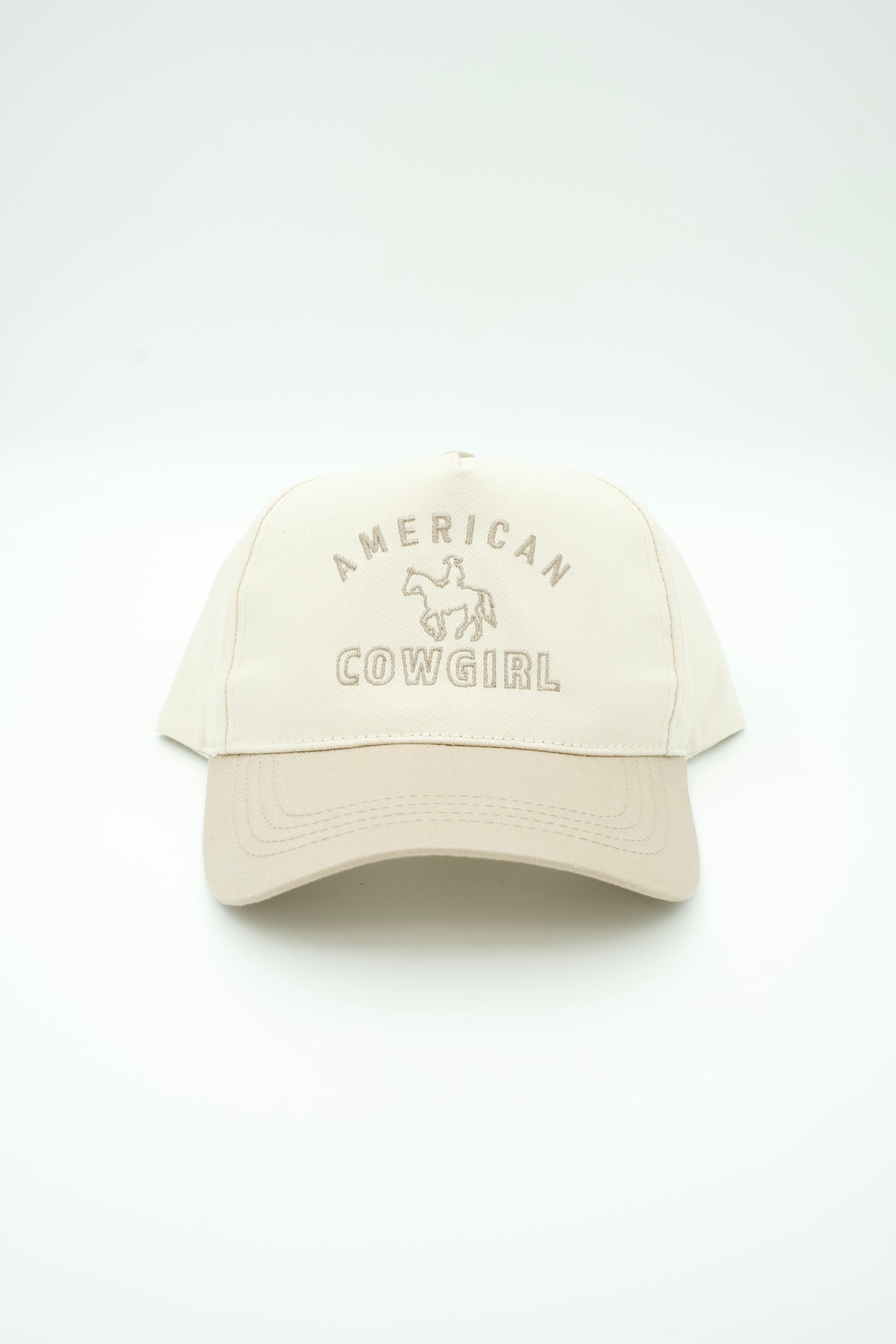 A cream-colored baseball cap with 'AMERICAN COWGIRL' and a cowboy graphic embroidered on the front, set against a plain white background.