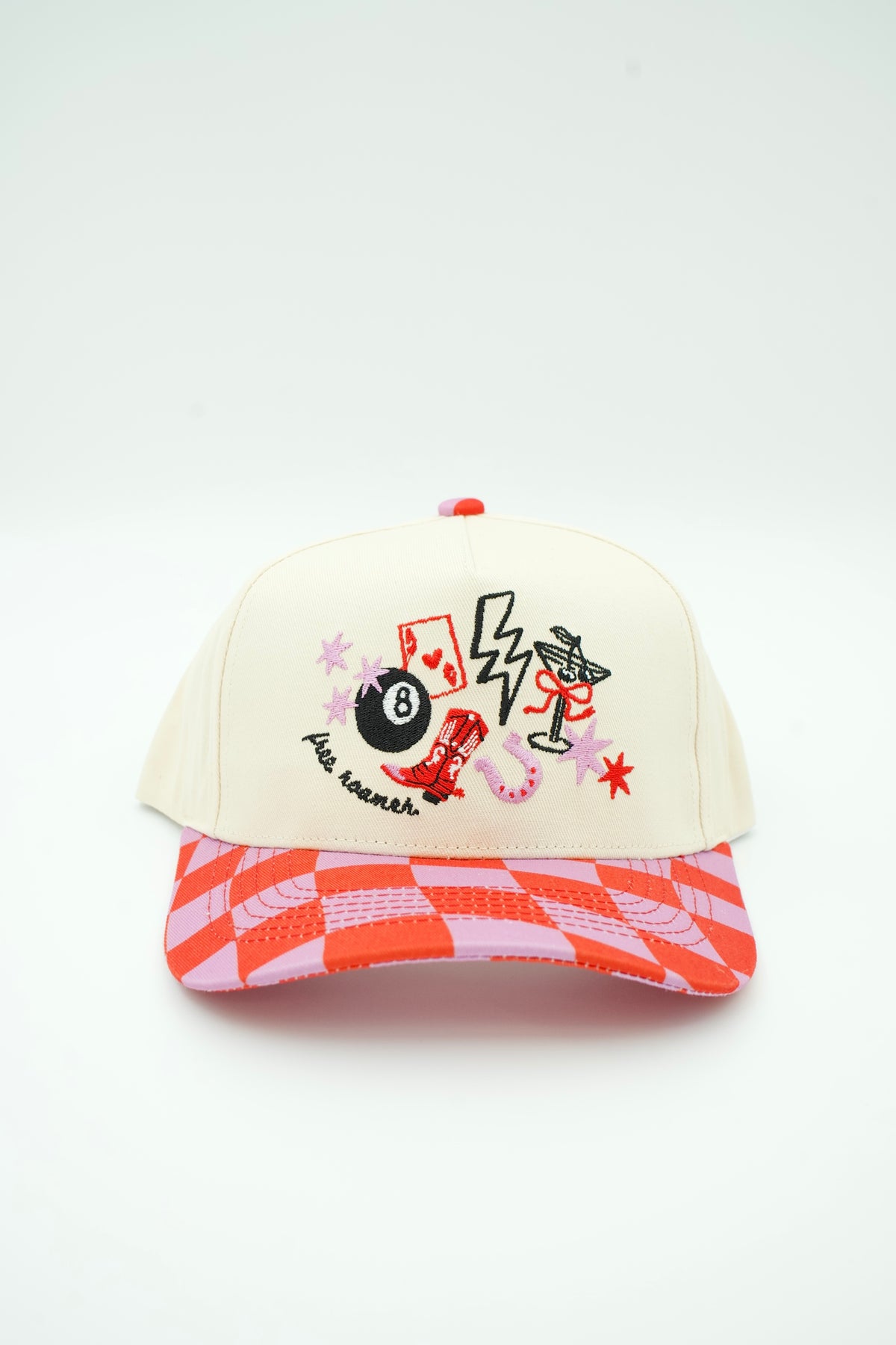 Front image of cream canvas trucker hat with "Free Roamer" embroidered and eight ball cowboy boot, horse shoe and ace card embroidered designs with a pink and red checkered bill. 