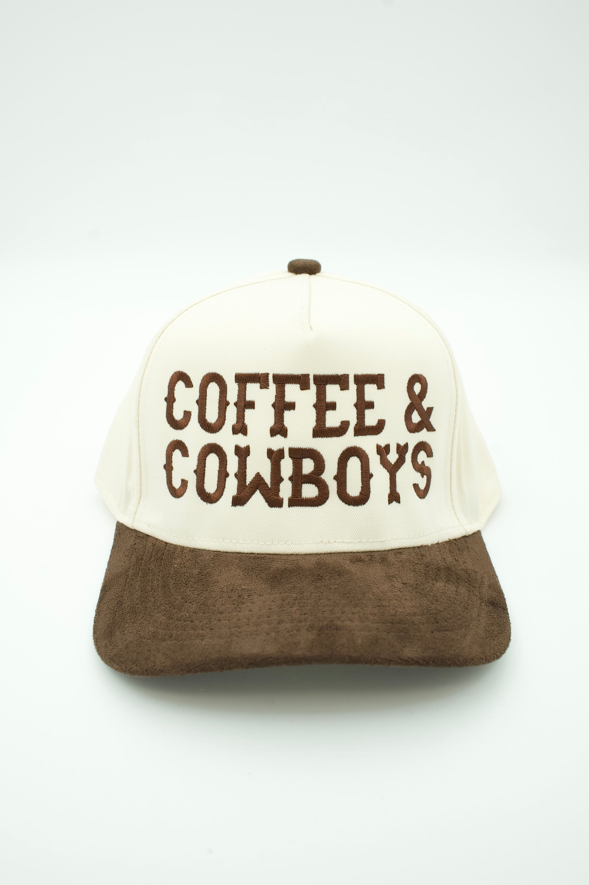 A trucker-style baseball cap with an off-white front panel and brim, brown mesh back, and brown suede-look brim. The front panel features the words 'COFFEE & COWBOYS' in brown distressed lettering.