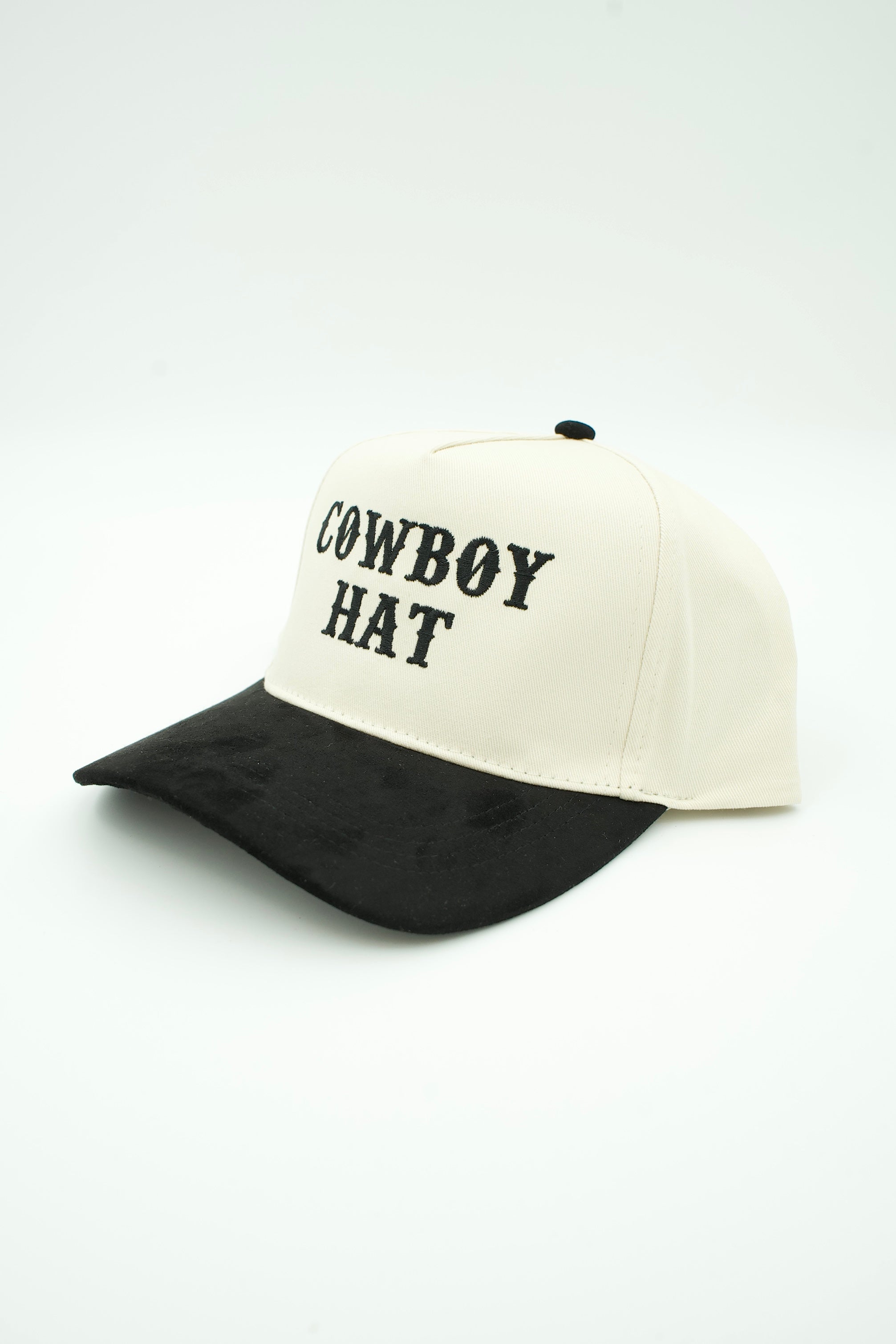 A two-tone baseball cap with an off-white crown and a black brim, featuring the text 'COWBOY HAT' embroidered in black on the front. The cap is photographed on a seamless white studio background.