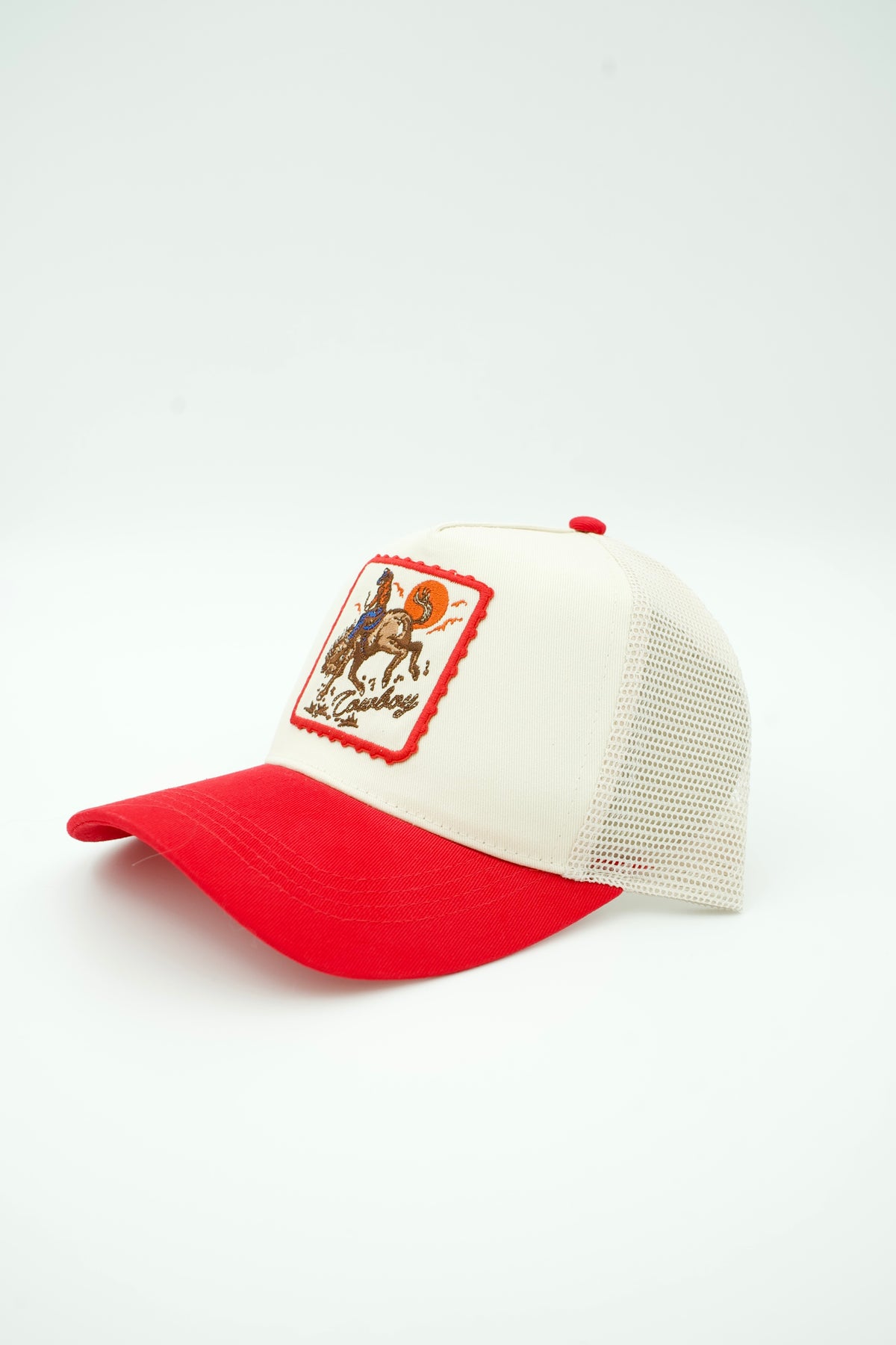 Front image of canvas trucker hat with embroidered "COWBOY" and a cowboy on a bucking horse with a sunset in the background with a red bill