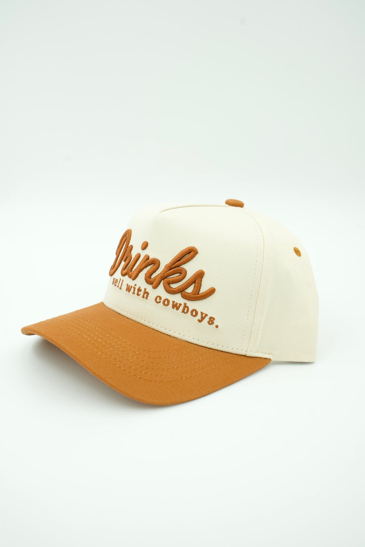 Side image of ivory canvas trucker hat with DRINKS WELL WITH COYBOYS embroidered in brown with brown bill