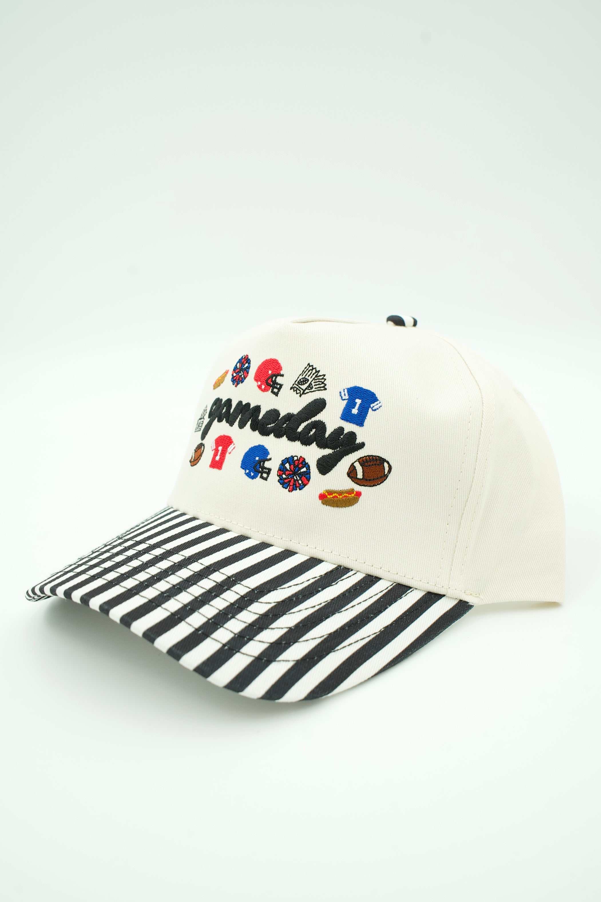 A baseball cap with an off-white crown, black and white striped brim, and colorful embroidered patches spelling 'Gameday' with sports icons on the front.