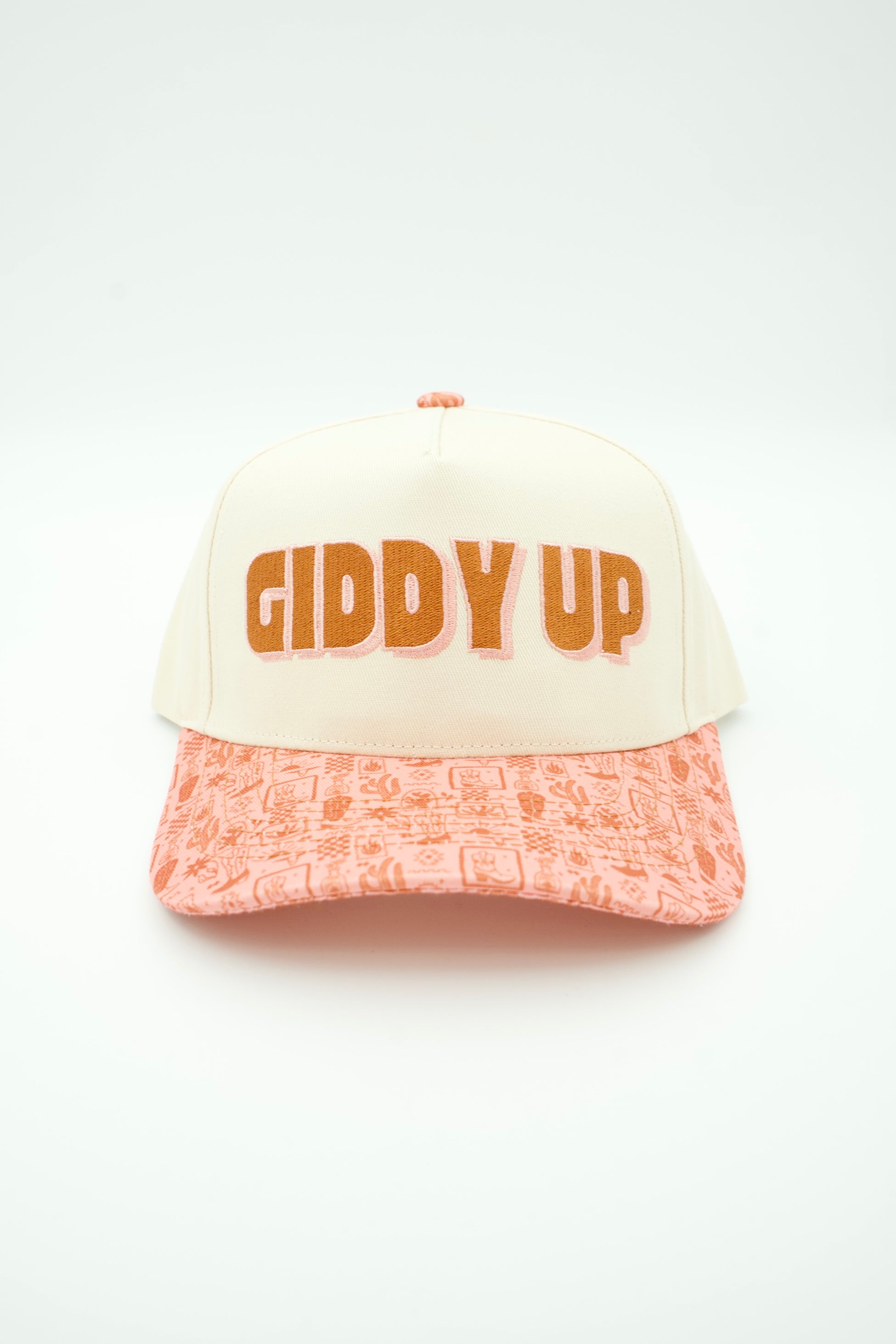 A trucker-style baseball cap with an off-white crown and a peach-pink patterned brim. The front features the text 'GIDDY UP' in orange with a pink outline.