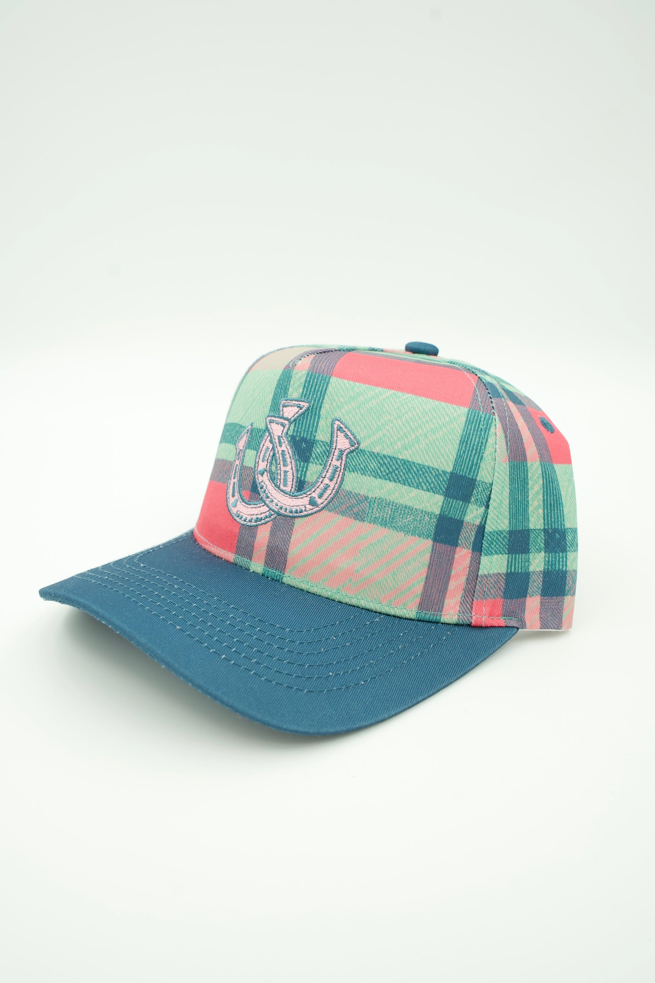 A baseball cap with a teal blue visor and a green, pink, and blue plaid patterned crown, featuring a white embroidered horseshoe logo on the front.