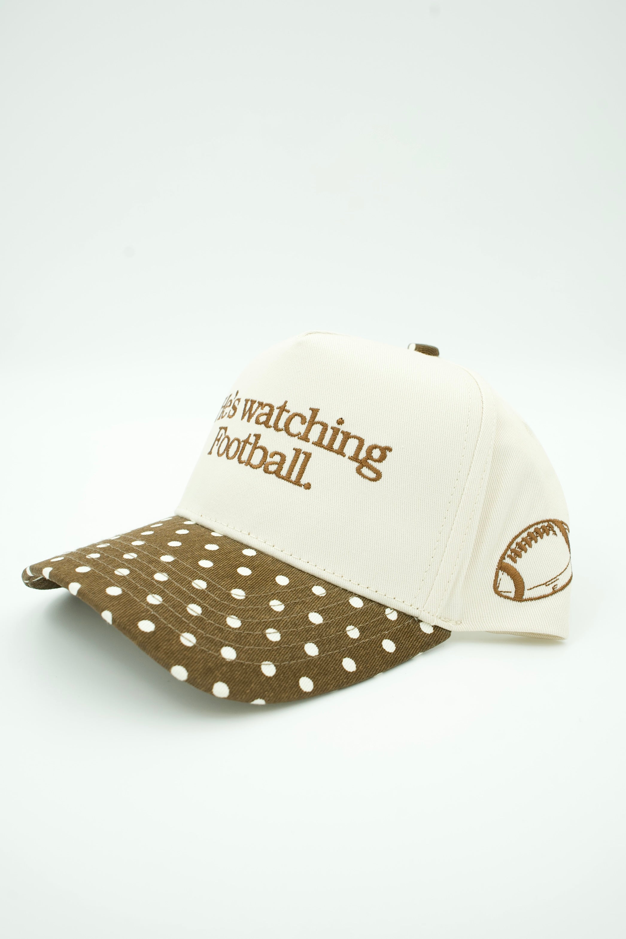 A baseball cap with an off-white crown and a brown brim covered in white polka dots. The crown features brown embroidered text reading 'I'm watching Football.