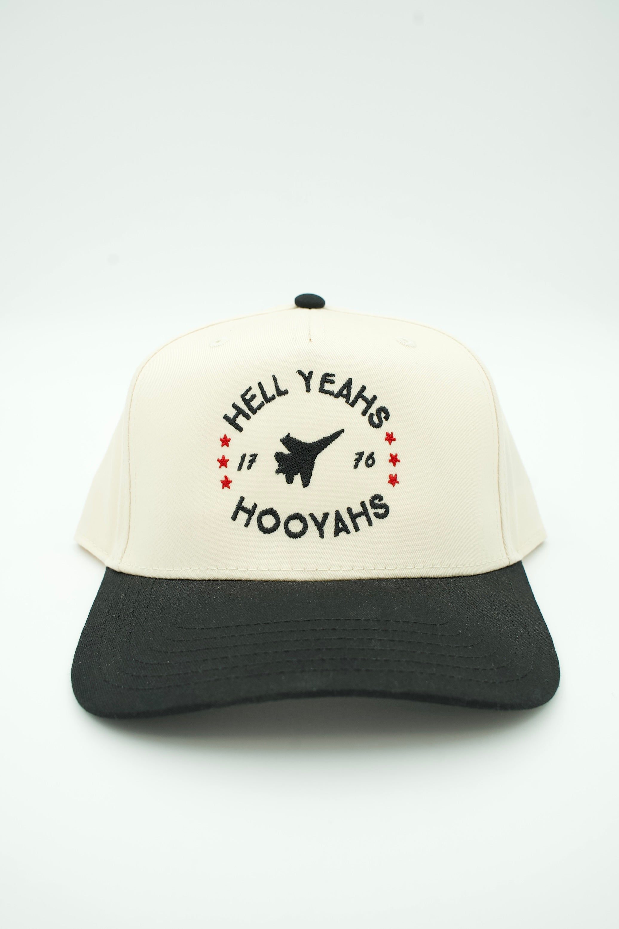 A structured trucker hat with an off-white crown and a black curved brim, featuring a black graphic with the text 'HELL YEAH'S HOOYAH'S' and small red stars on the front.