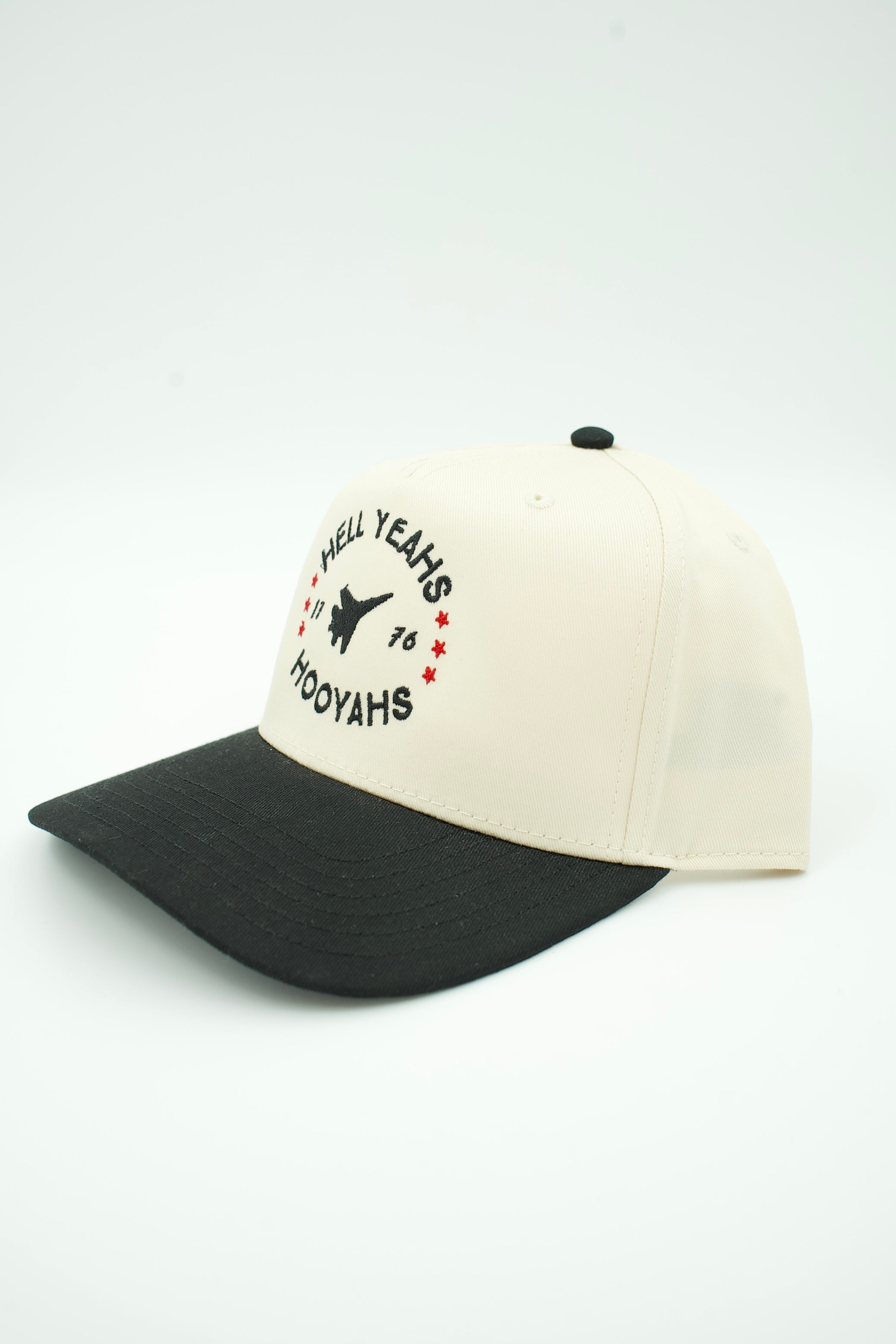 A baseball cap with an off-white crown and a black curved brim, featuring a black embroidered graphic on the front that reads 'ALL YEAHS 16 HOOYAHS' with a silhouette and red stars.