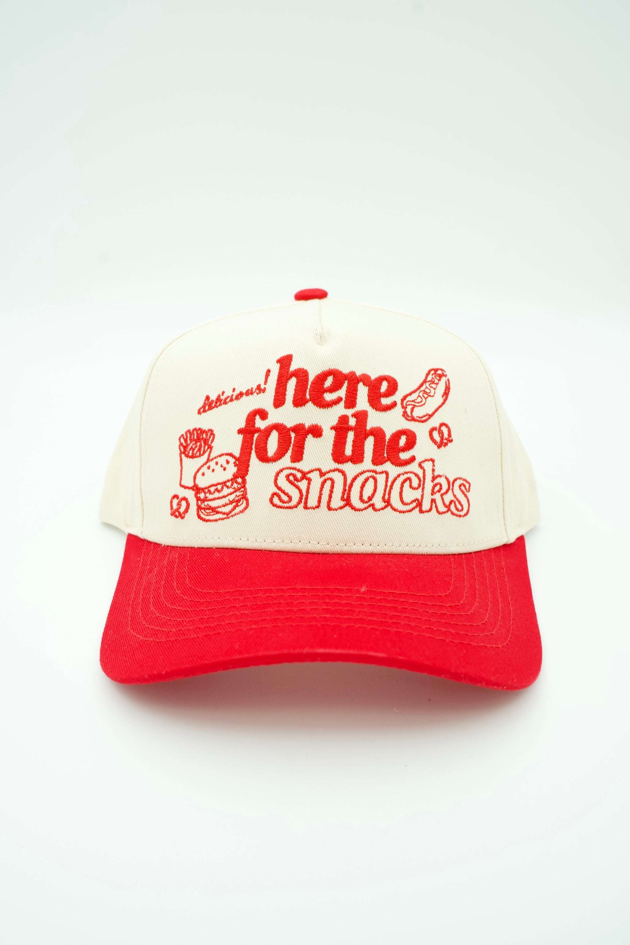 A red and off-white trucker cap with red embroidered text reading 'Delicious here for the snacks' and small food illustrations, shown against an off white background.