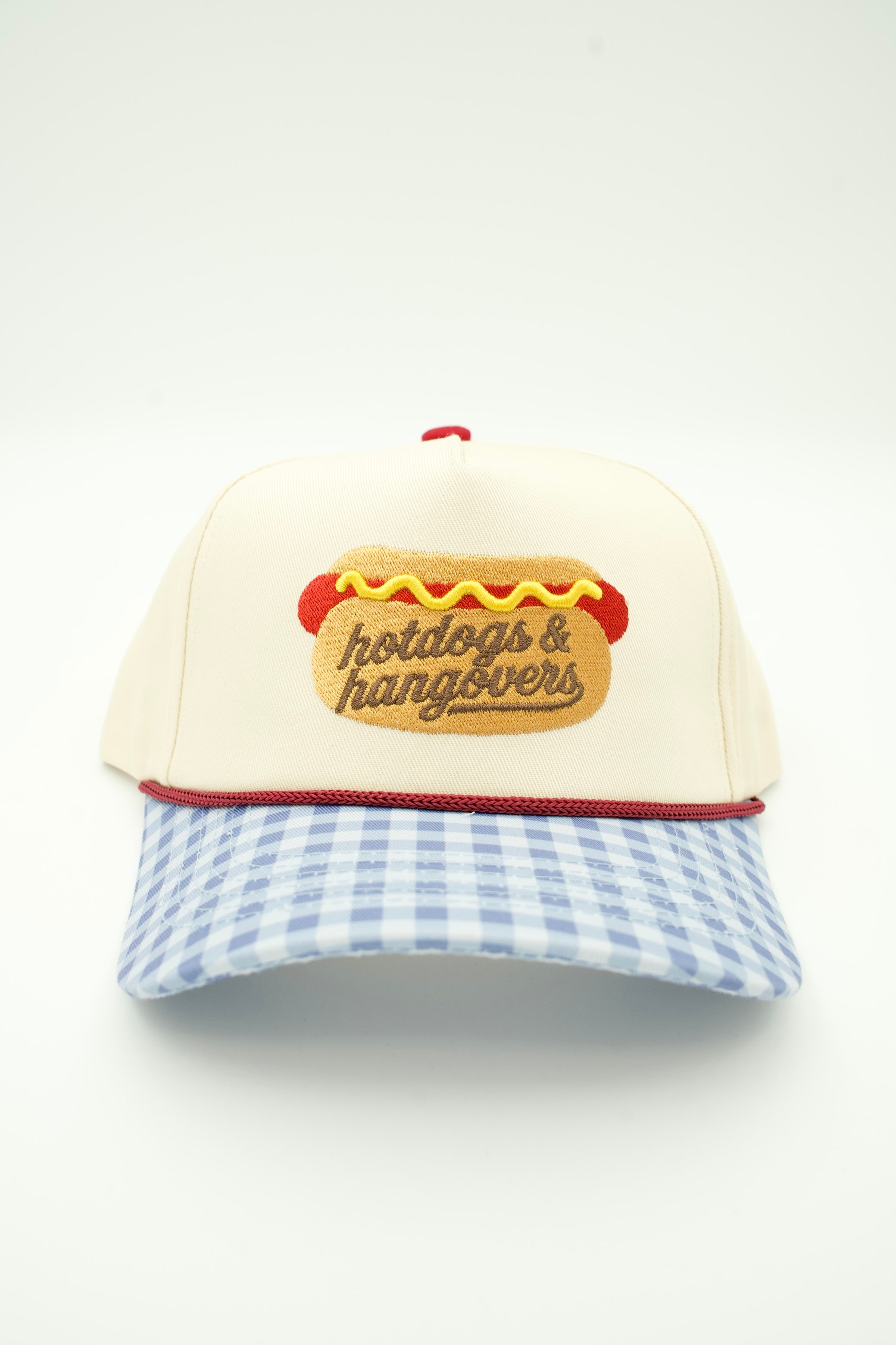 A baseball cap with an off-white crown, a light blue and white gingham brim, and a red embroidered hotdog patch on the front with the text 'hotdogs & hangovers'.