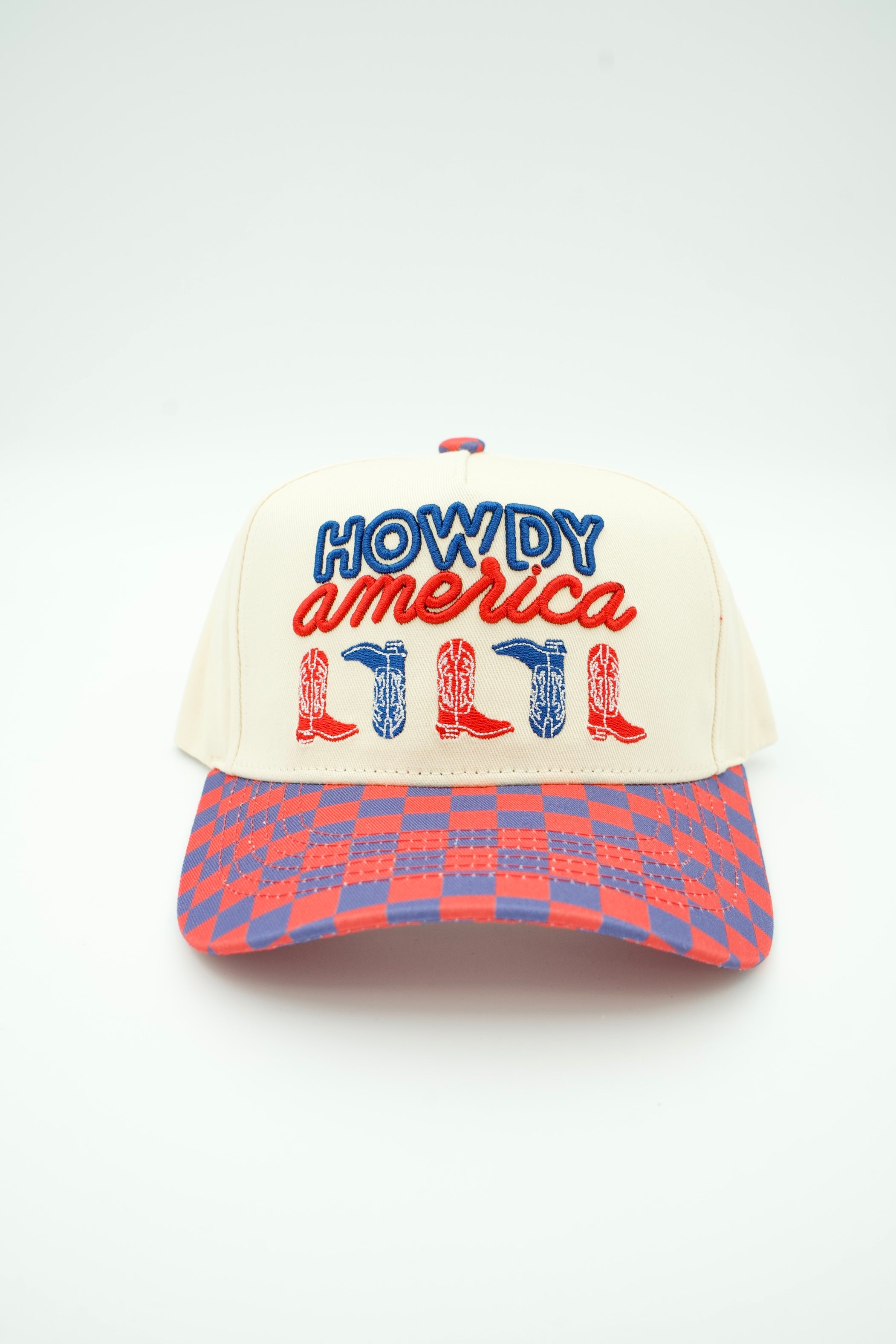 A baseball cap with an off-white crown featuring 'HOWDY america' embroidered on the front in blue and red, with red and blue cowboy boots below. The brim has a red and blue checkered pattern.