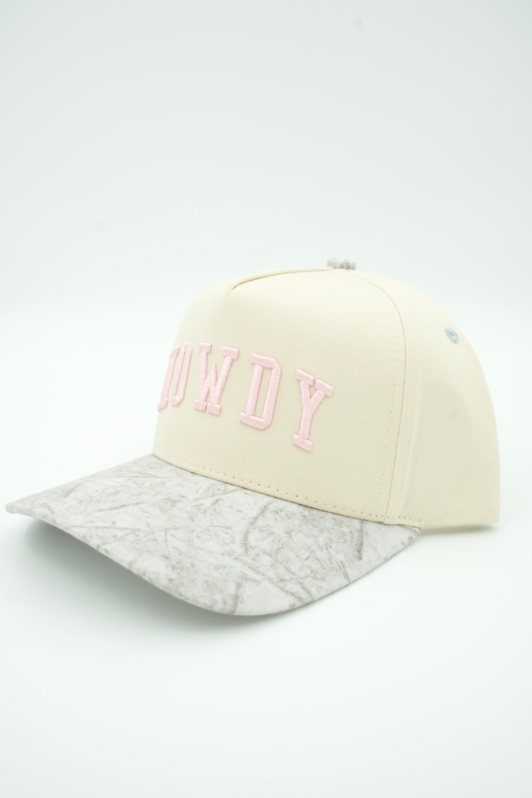 A cream-colored baseball cap with a light gray camouflage-patterned visor and pink embroidered lettering on the front that reads 'COWDY'.