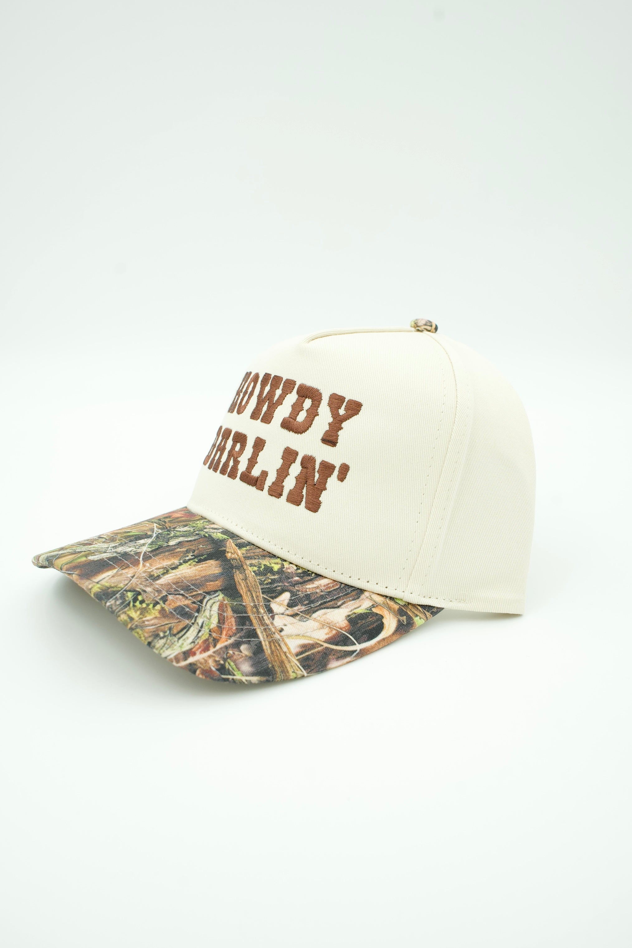 An off-white baseball cap with brown embroidered text reading 'COWDY BERLIN' on the front, featuring a camouflage patterned brim, photographed on a clean white background.