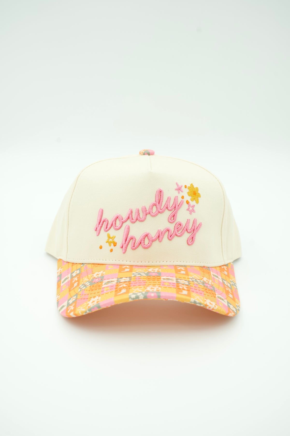 A cream-colored baseball cap with pink embroidered 'howdy honey' text and small yellow flowers on the front, featuring a pastel multicolor patterned visor.