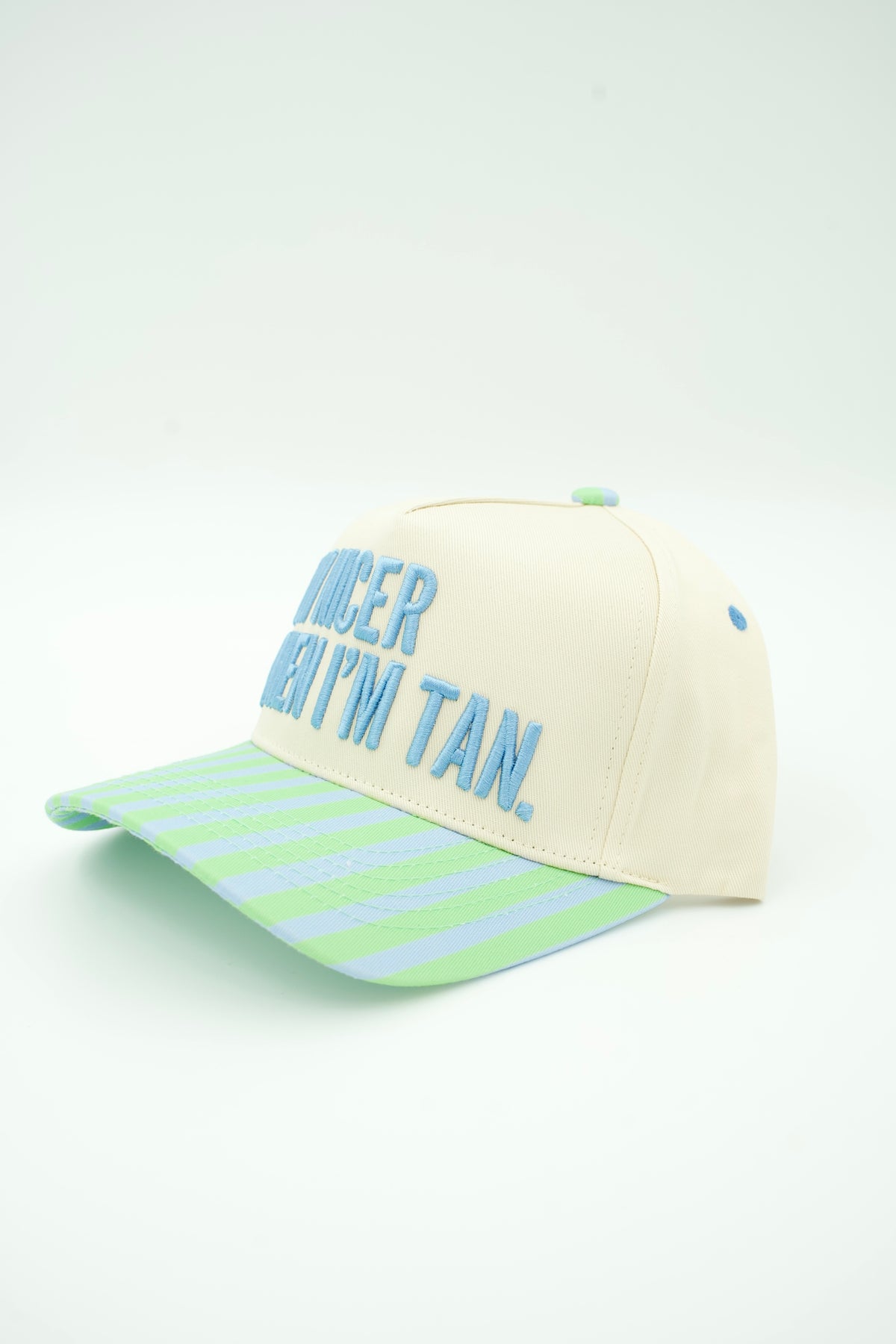 Side image of a cream canvas trucker hat with "I'M NICER WHEN I'M TAN" embroidered on it with a baby blue and mint green striped bill