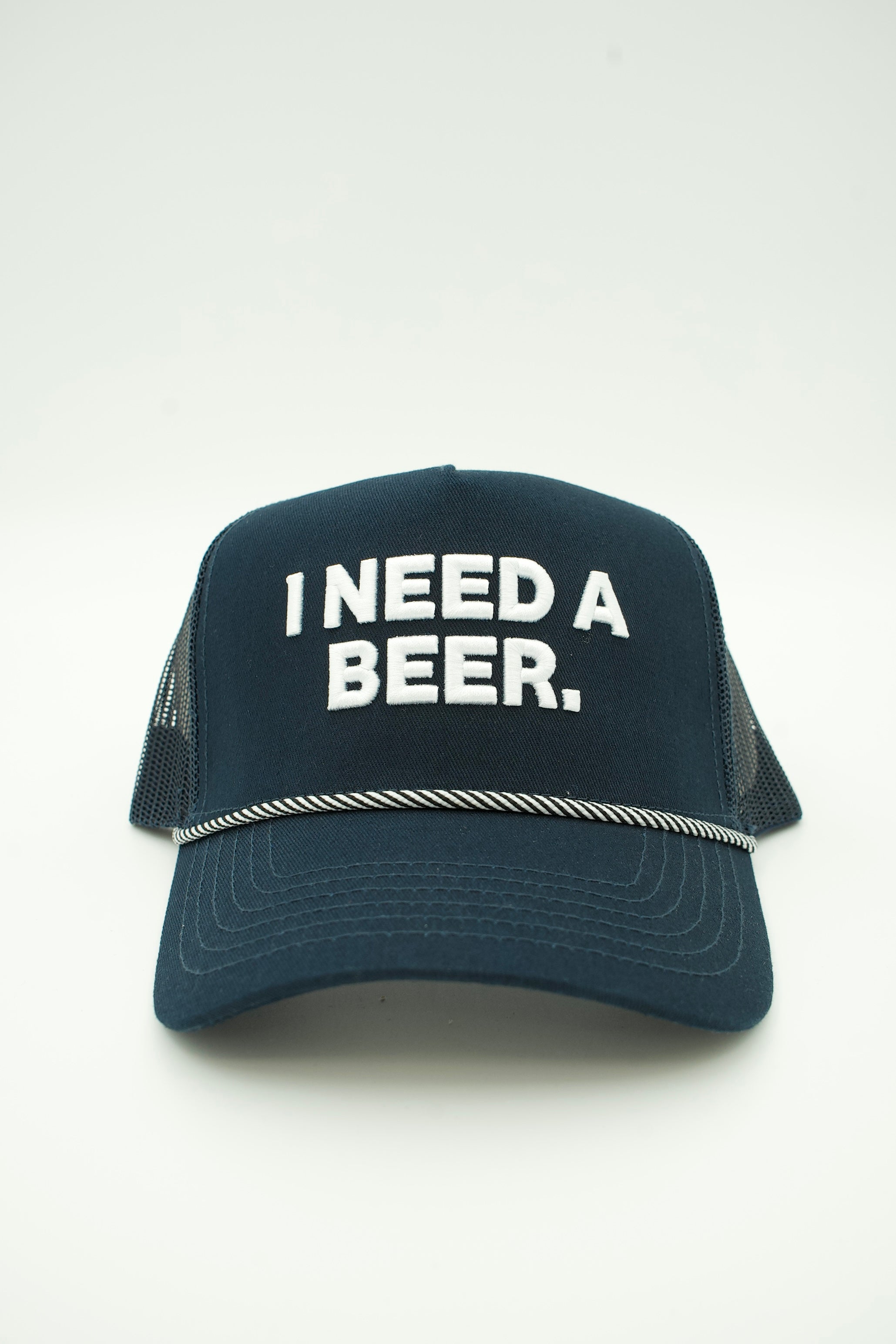 A dark navy blue trucker hat with white embroidered text reading 'I NEED A BEER.' on the front, set against a plain light gray background.