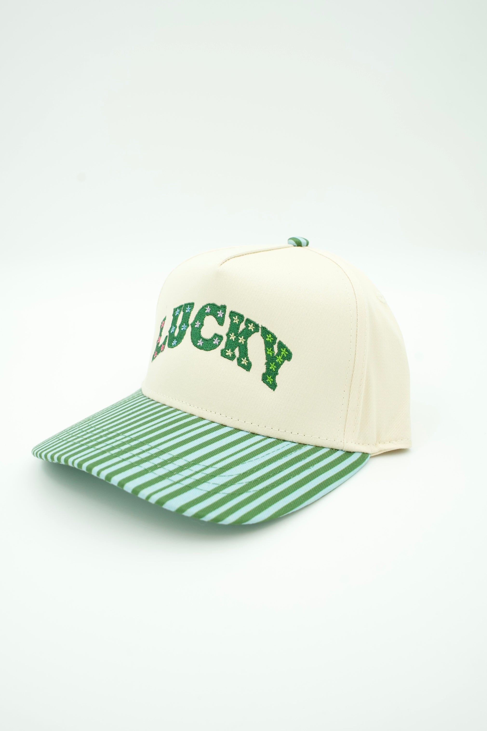 An off-white baseball cap with a green and white striped visor and green embroidered 'LUCKY' lettering on the front, set against a plain white background.